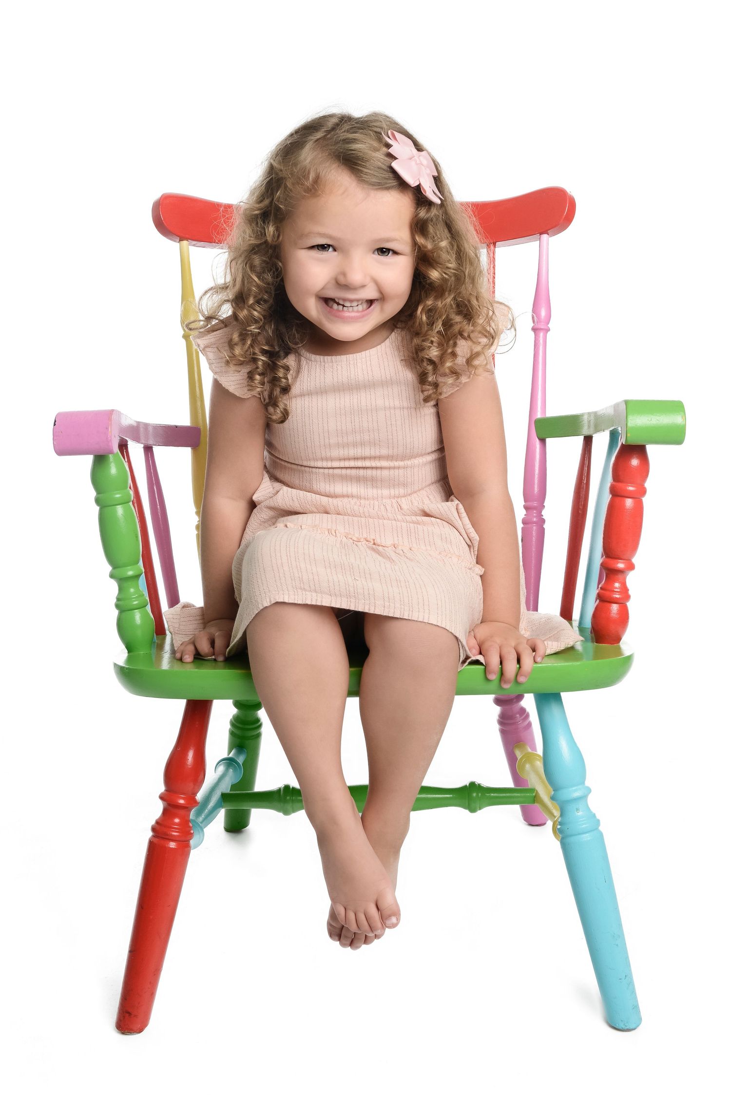 Cheerful pose on whimsical multicolored wooden chair against white background.