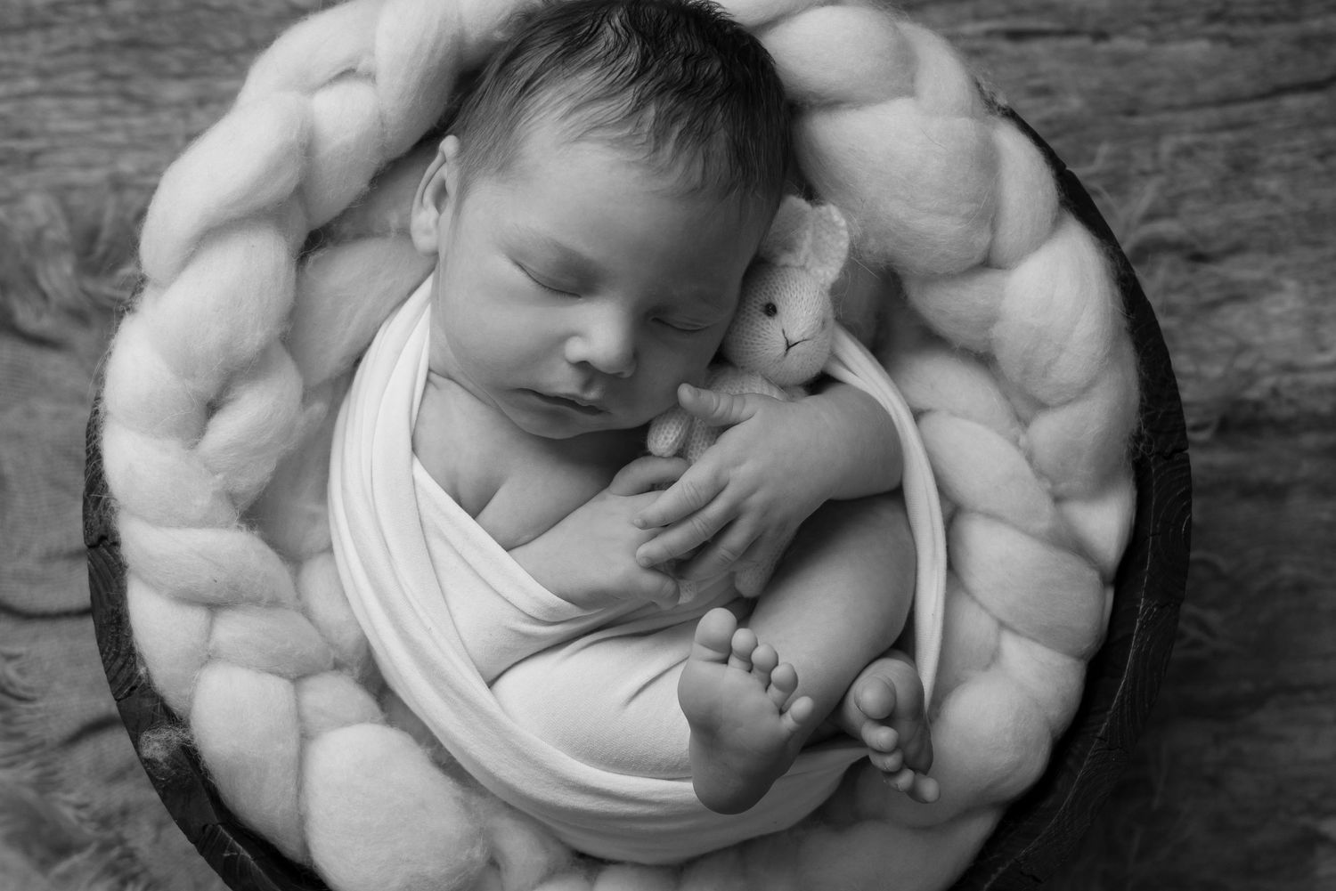 Monochrome portrait of sleeping newborn curled up in round basket.