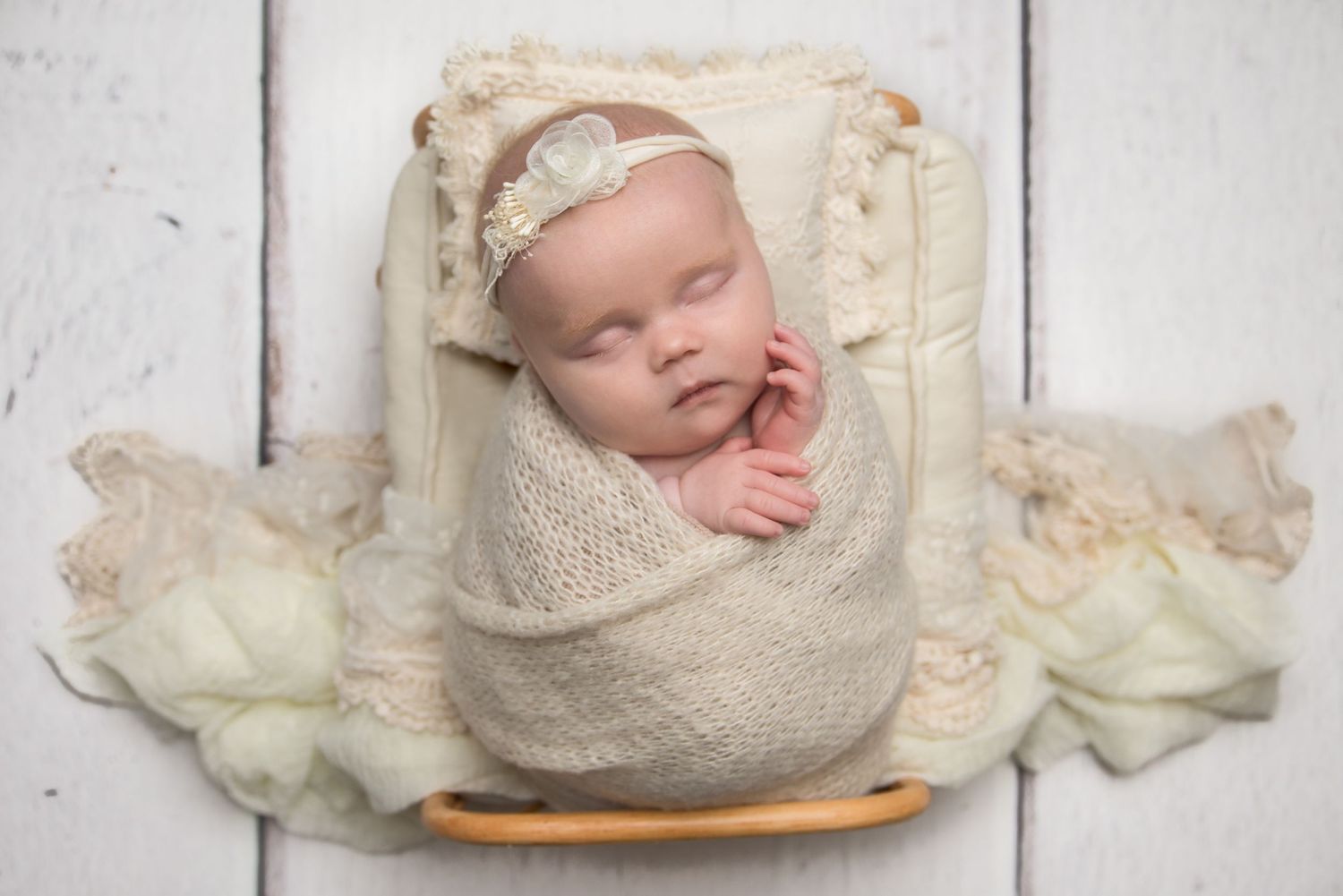 Peaceful newborn photography on white wooden backdrop with cream colored wraps.