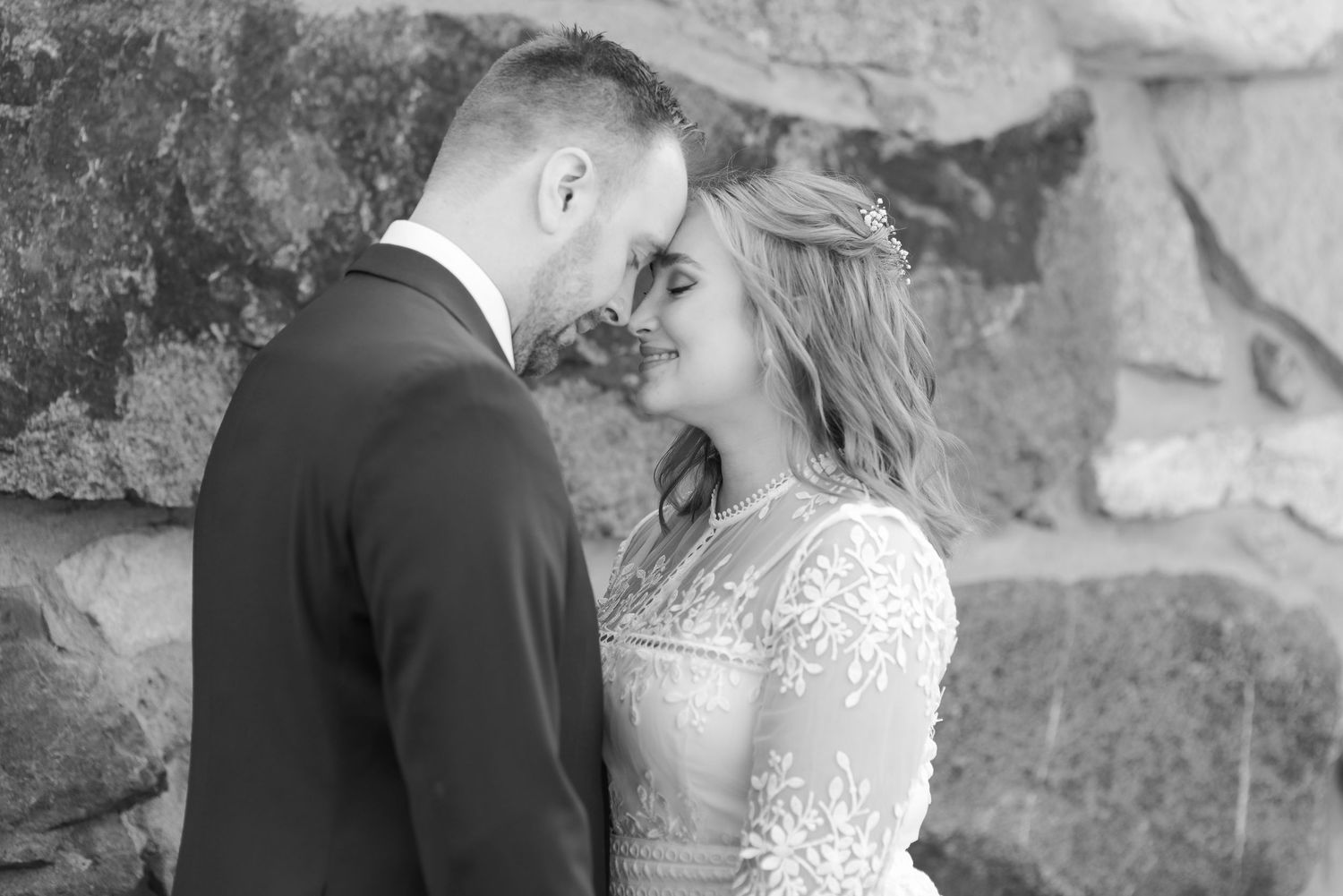 Black and white portraits of couple against textured stone wall background.