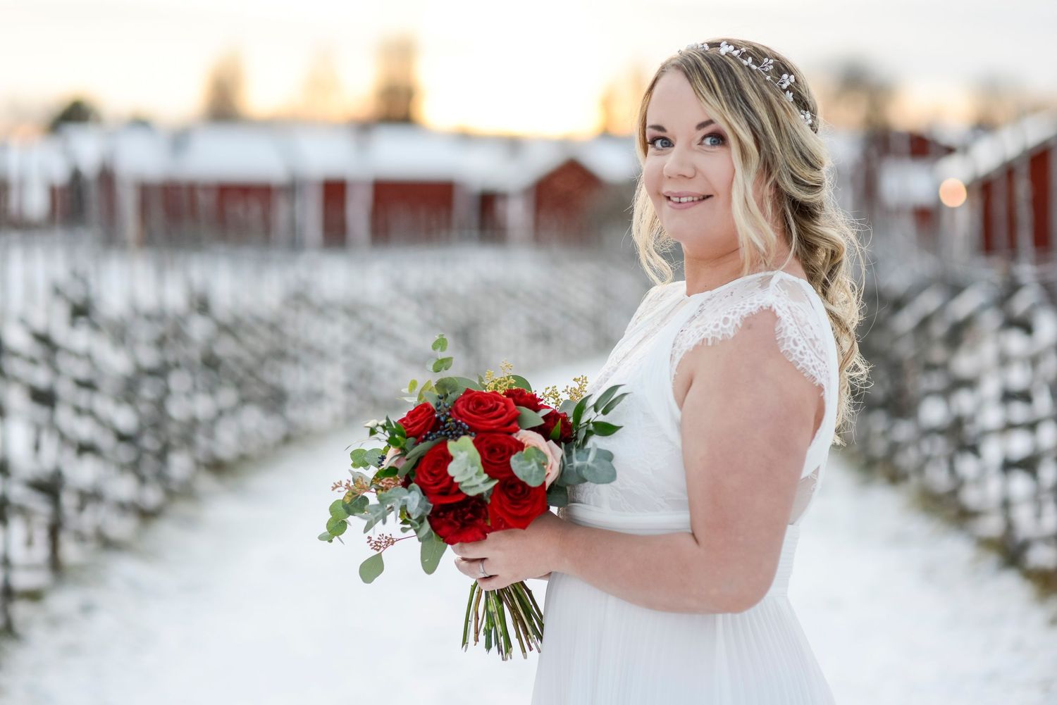 Winter wedding photography featuring white gown and red florals in snowy setting.