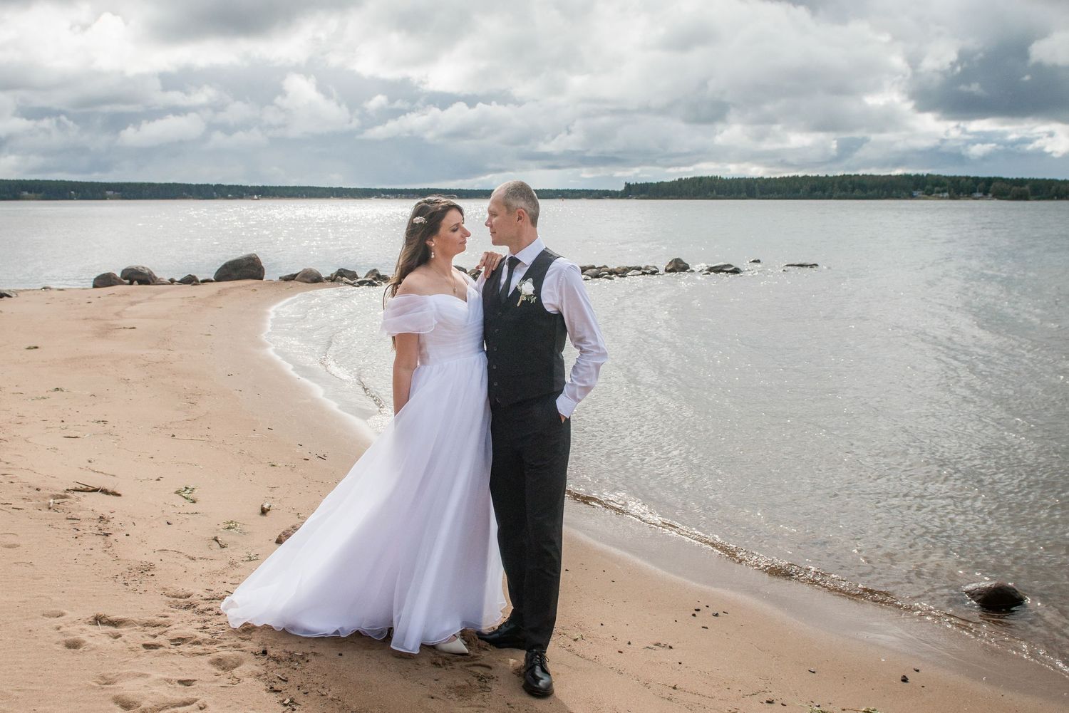 Wedding couple posing on a beach with cloudy skies and waves in the background.