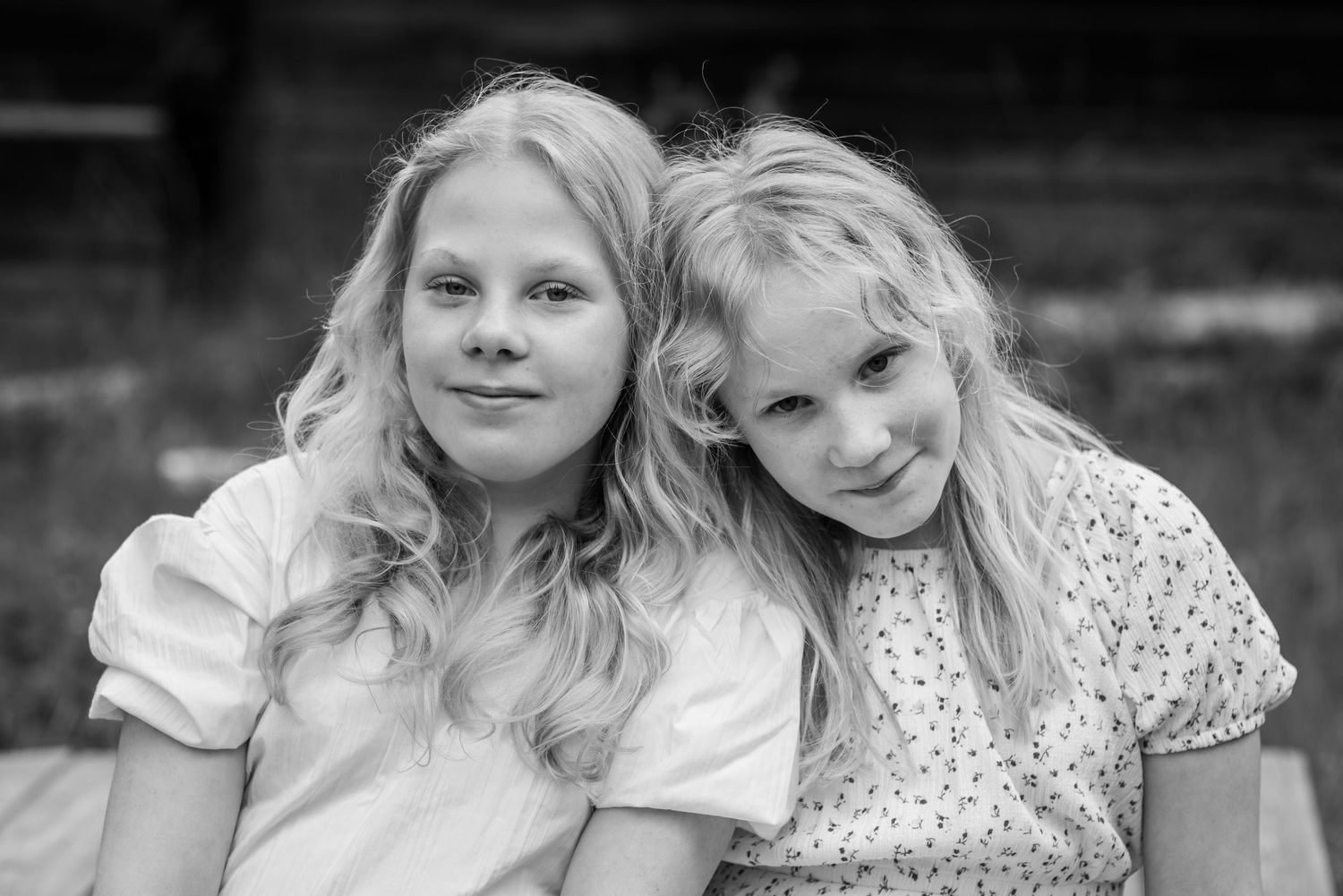 Two blonde girls smiling and posing together outdoors in a black and white portrait photo.