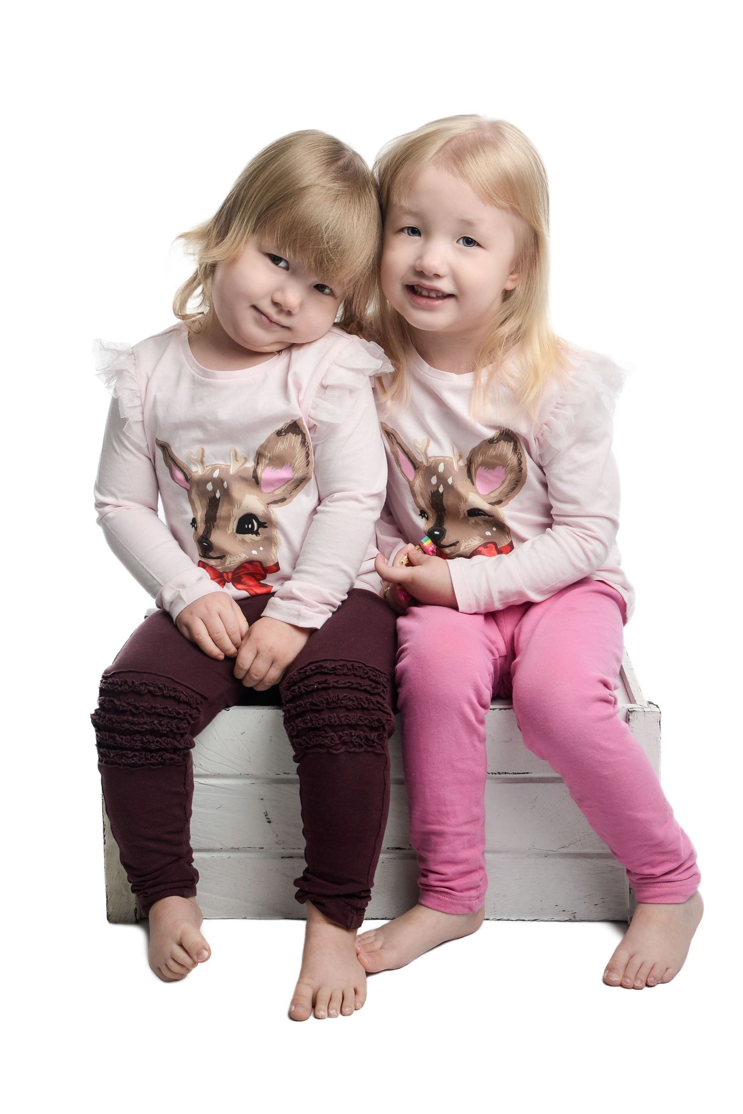 Two children in pink tops and colored pants sitting together on bench.