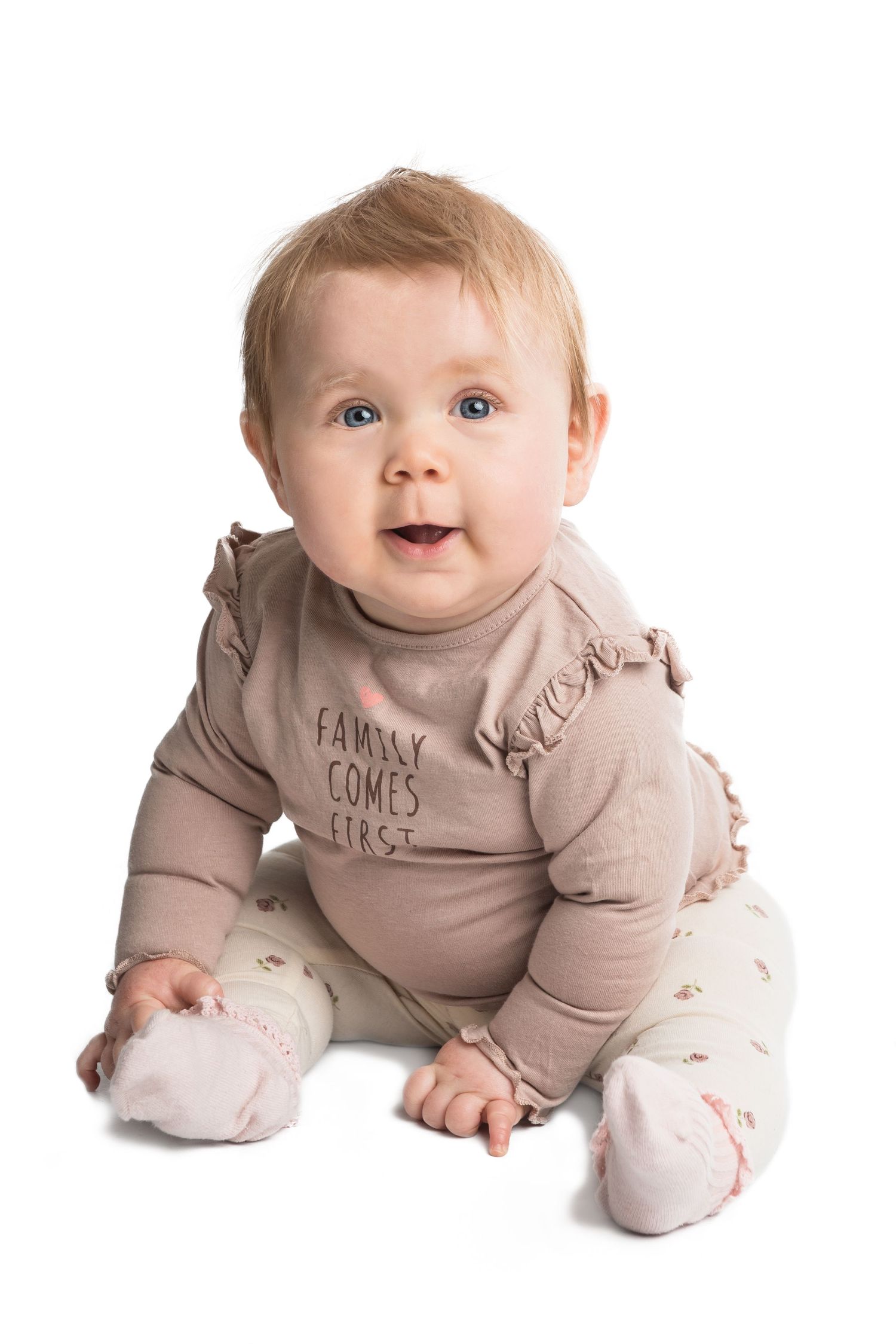 Baby wearing beige ruffled outfit sitting on white background.