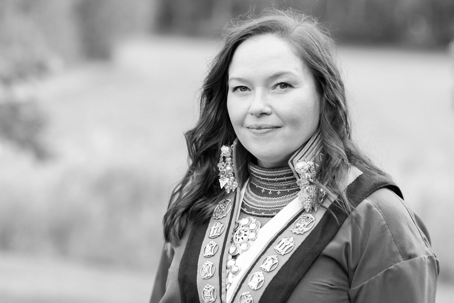 Black and white portrait of a woman in traditional Indigenous attire with decorative earrings outdoors.