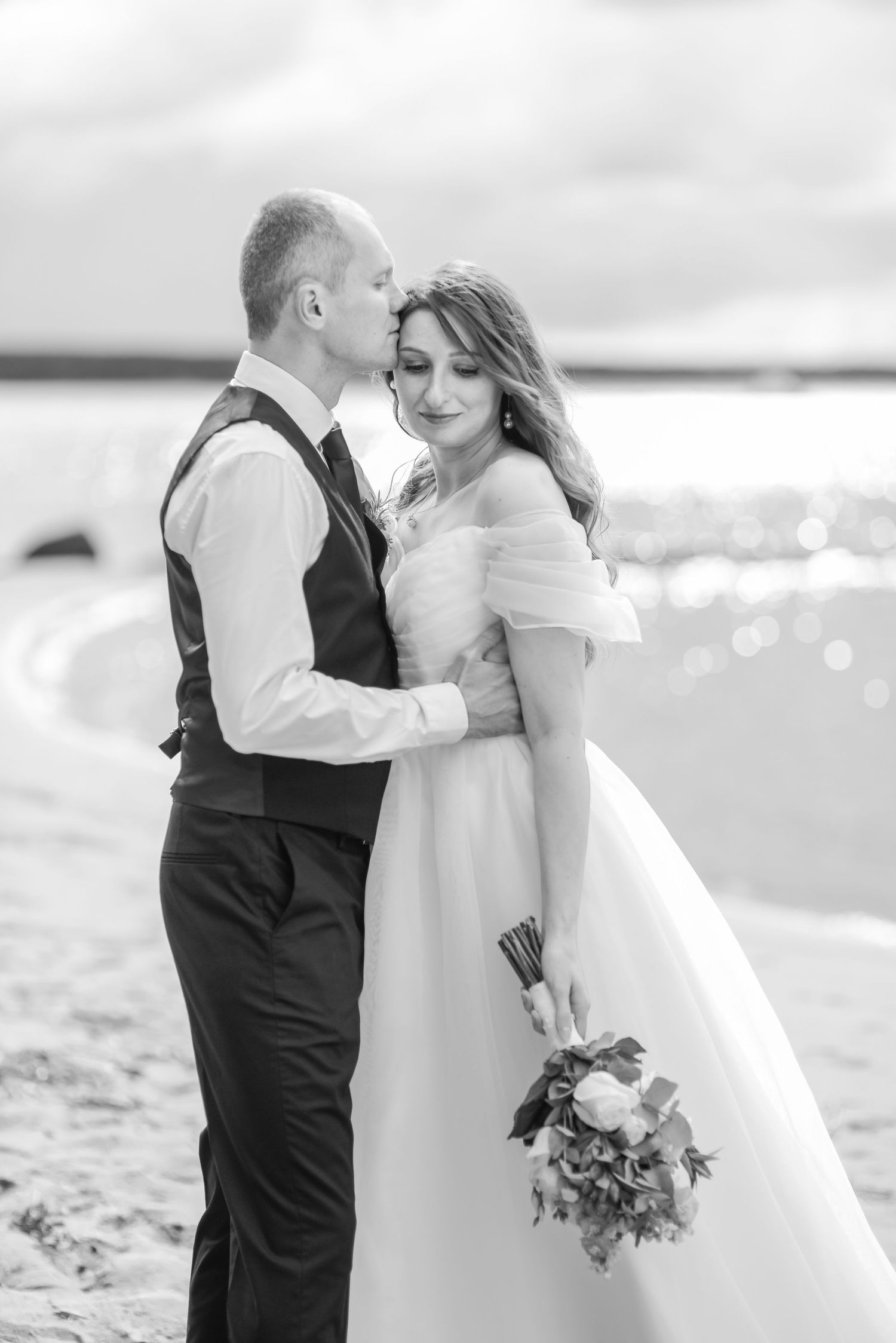 Romantic beach wedding portraits with couple embracing on sandy shore.