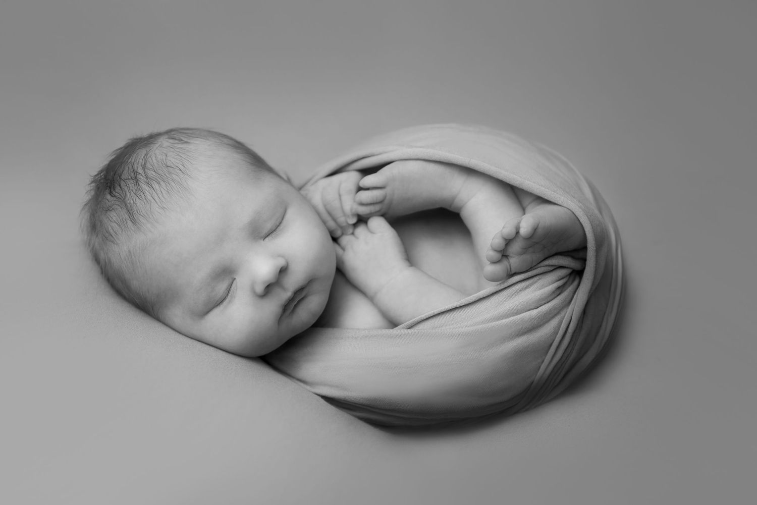 Black and white portrait of sleeping infant swaddled in light fabric.