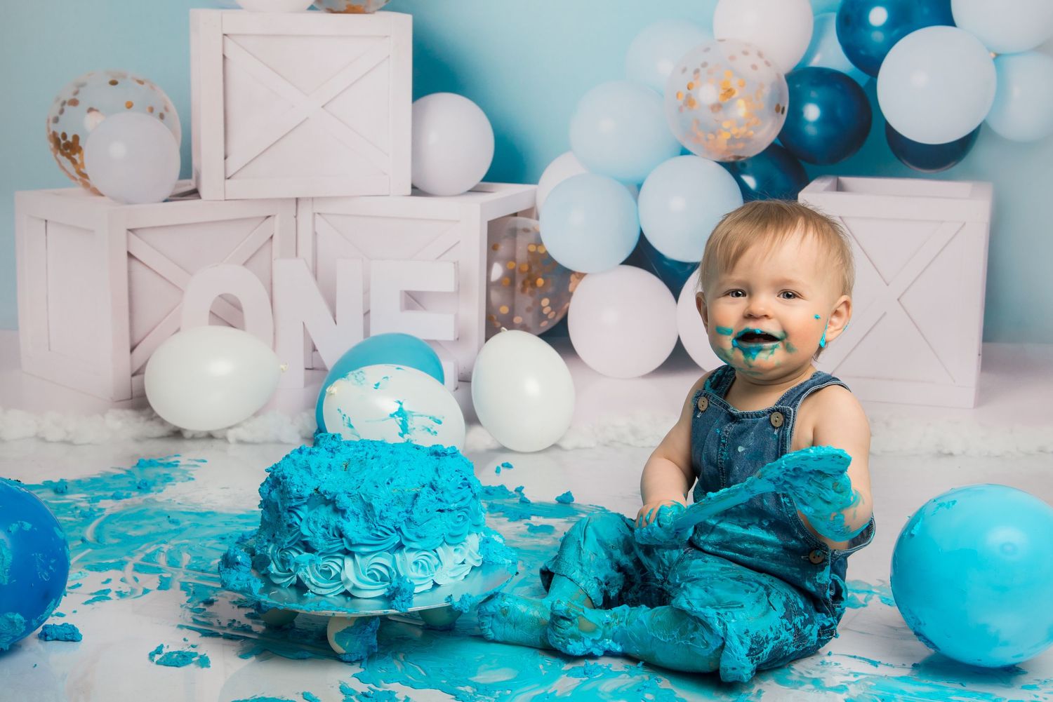 A messy cake smash photo session with bright blue frosting and balloons creating a playful scene.