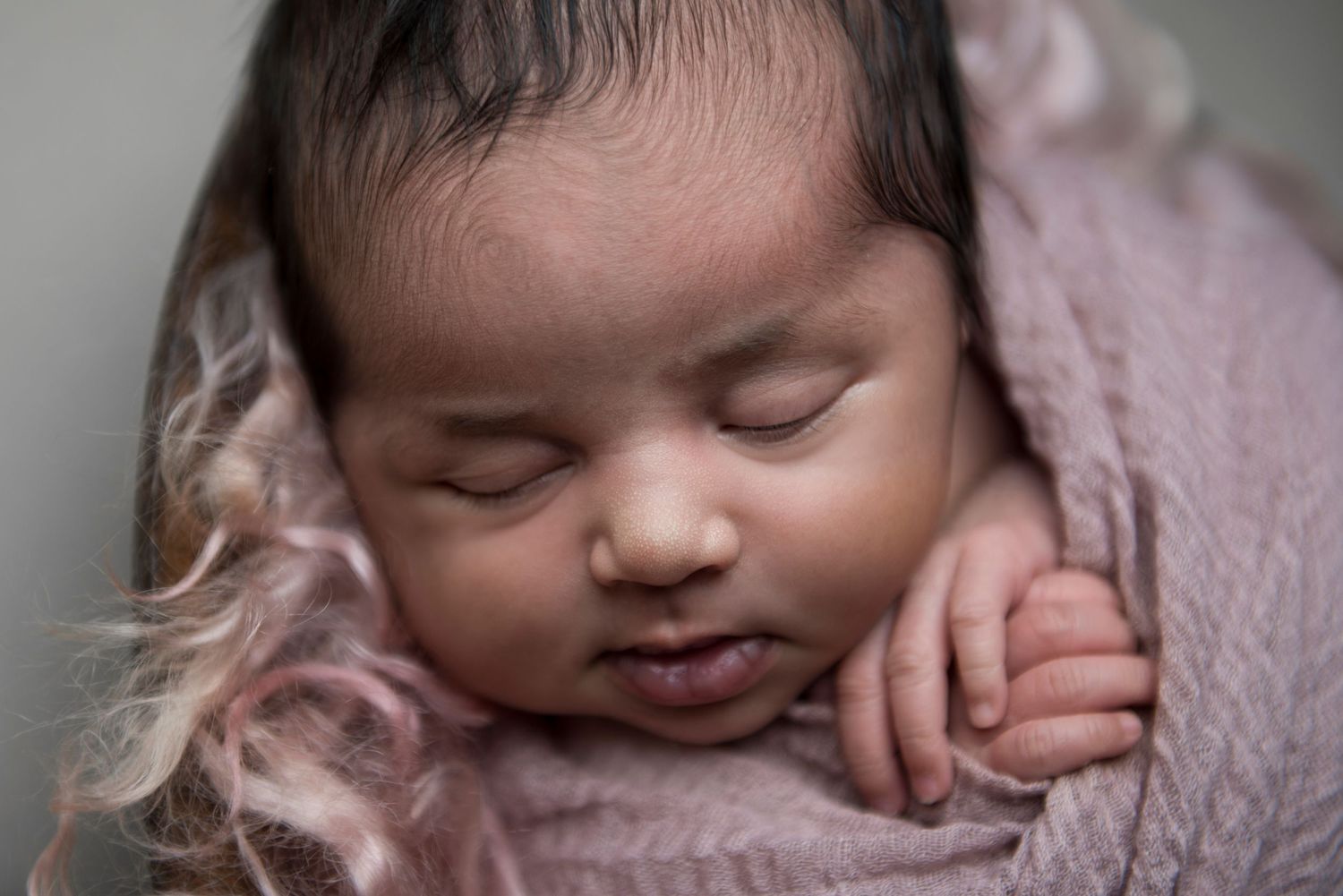 Sleeping newborn wrapped in soft pink blanket in dreamy portrait setting.