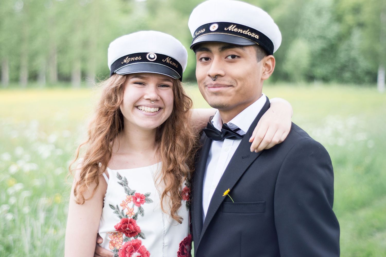 Couple in graduation attire sharing a romantic moment in a summer meadow.