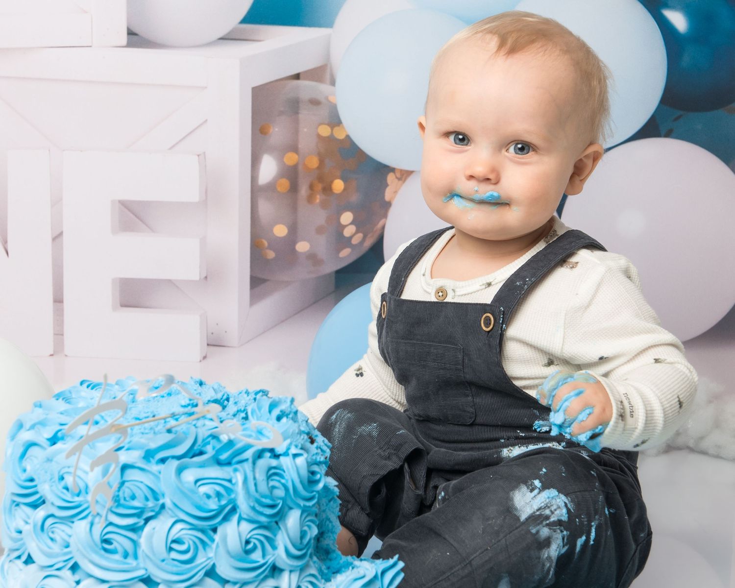 First birthday cake smash photography with blue frosted cake and white balloon decorations.