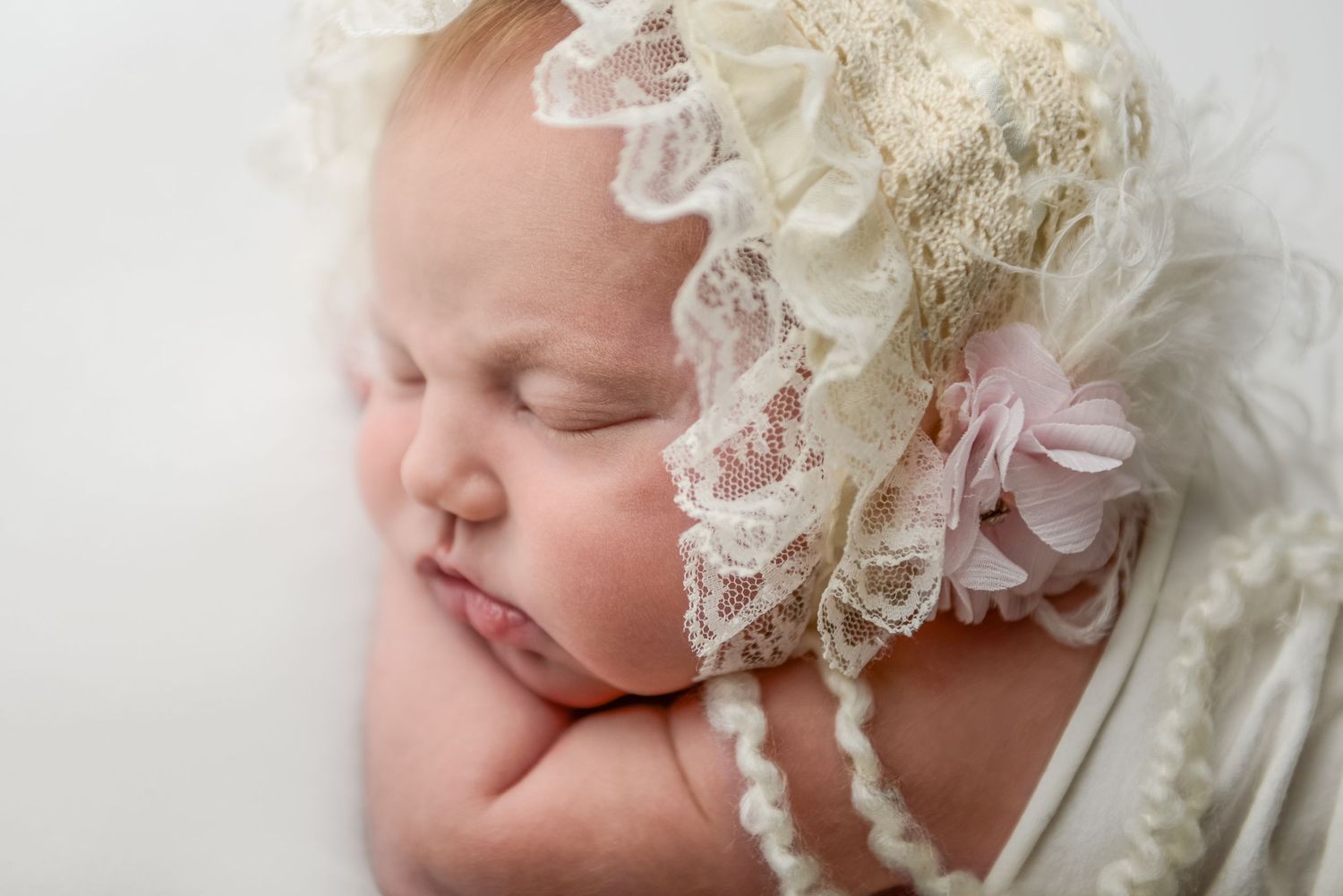 Newborn baby sleeping peacefully in vintage white lace bonnet.