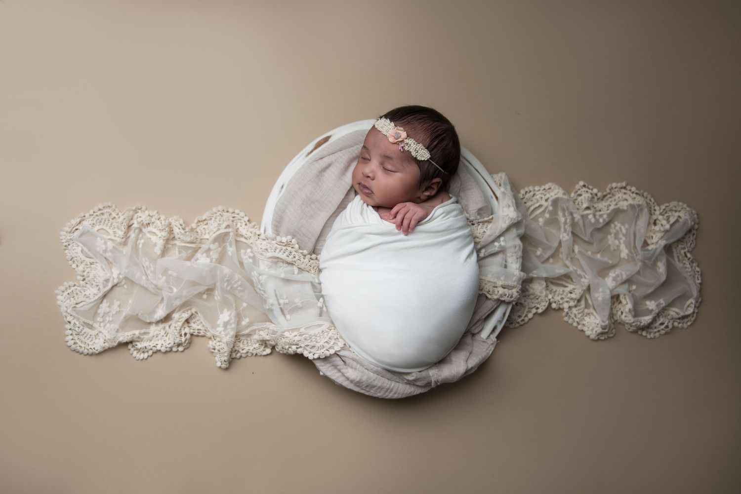 Professional newborn photography session with white lace and neutral backdrop.