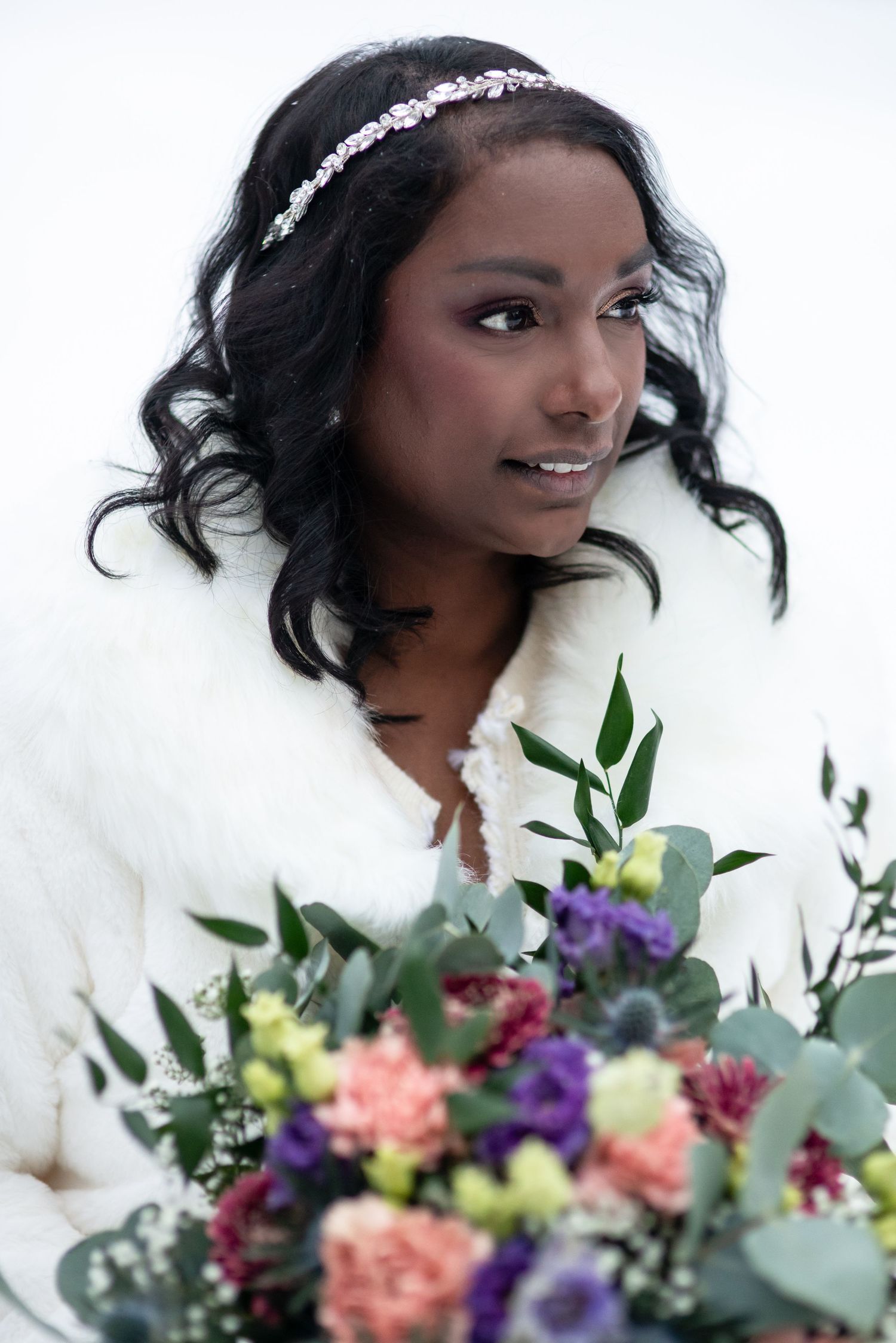 A winter bridal portrait features a colorful bouquet with pink and purple flowers against a snowy background.
