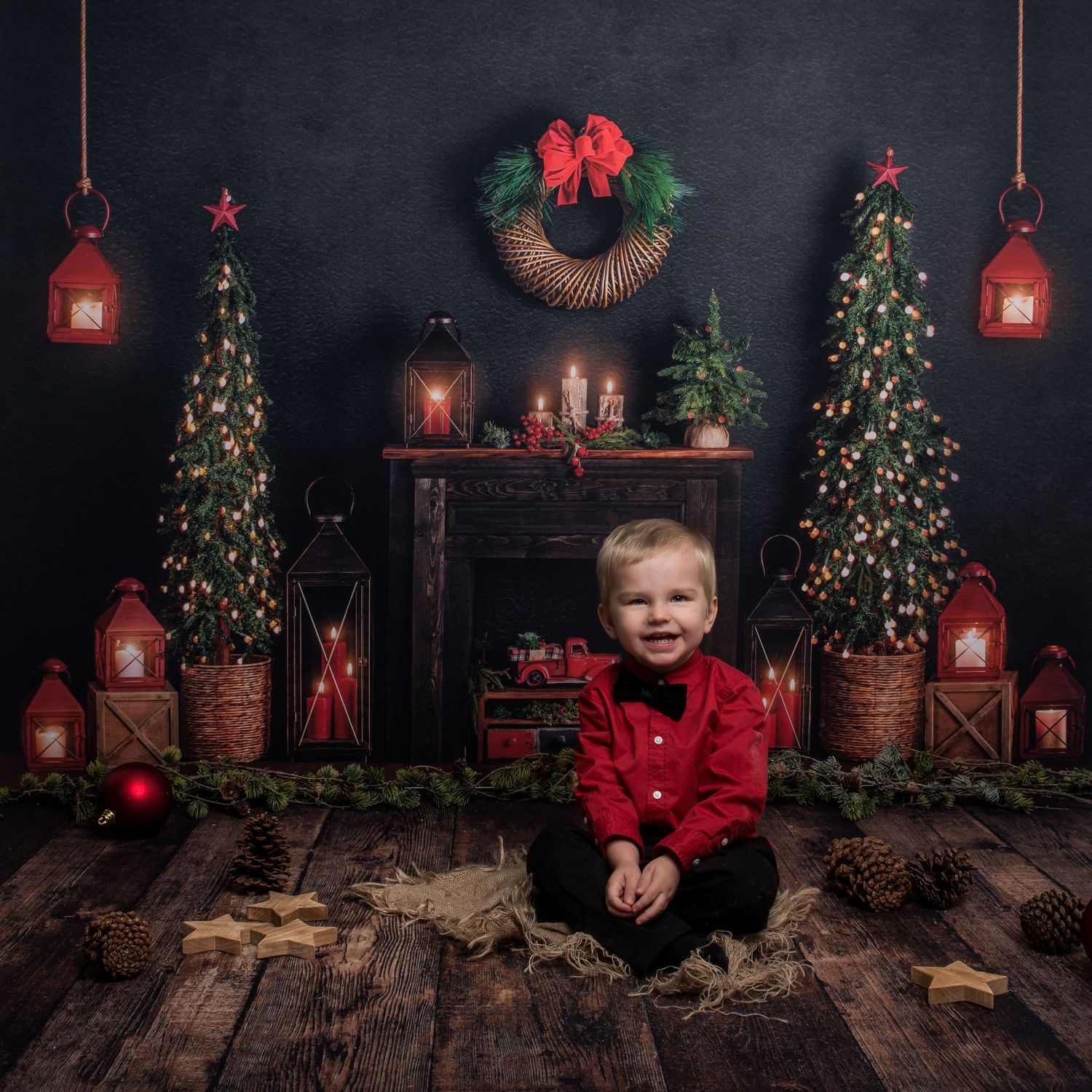 Dark and moody Christmas photo setup with glowing lanterns and decorated evergreen trees.