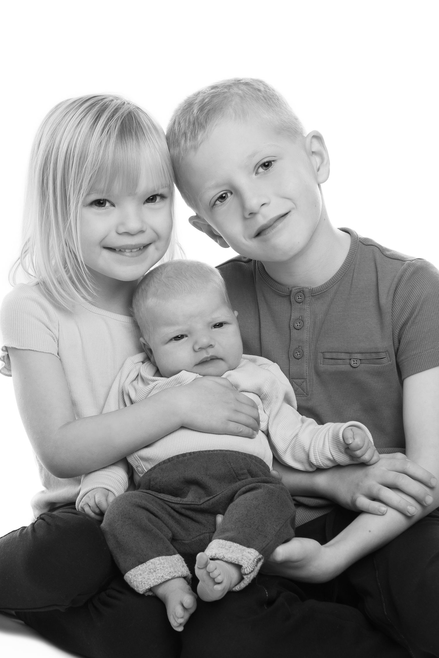 High-key family portrait series showing siblings bonding with newborn on white background.