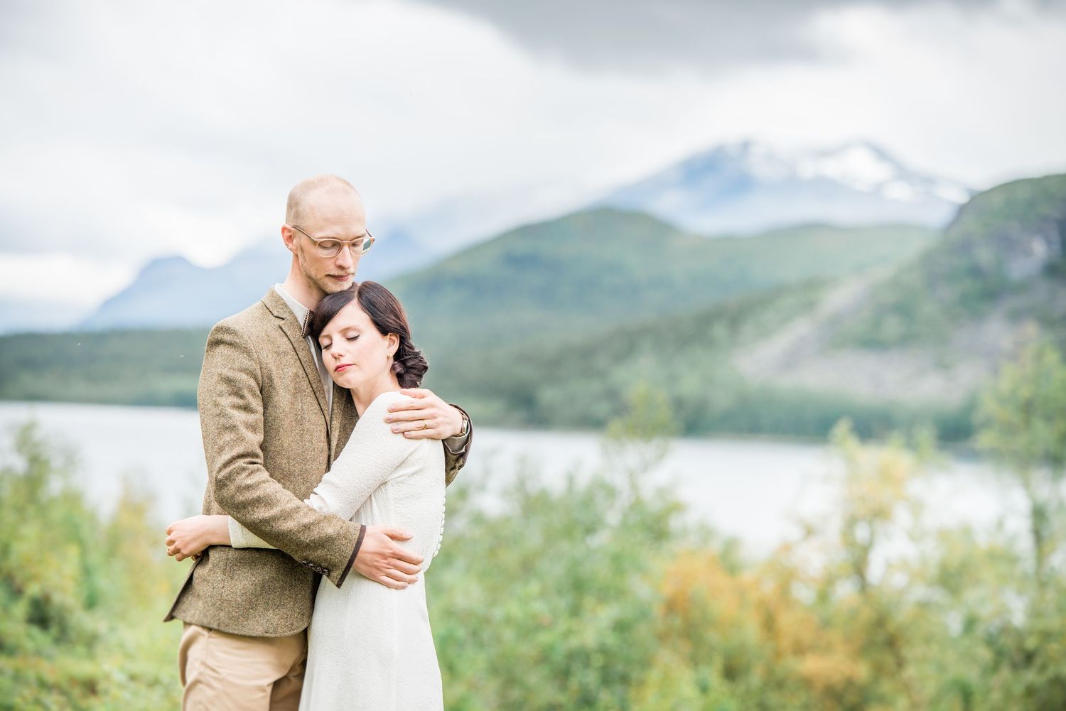 A romantic embrace against a mountain lake backdrop with snow-capped peaks and autumn foliage.