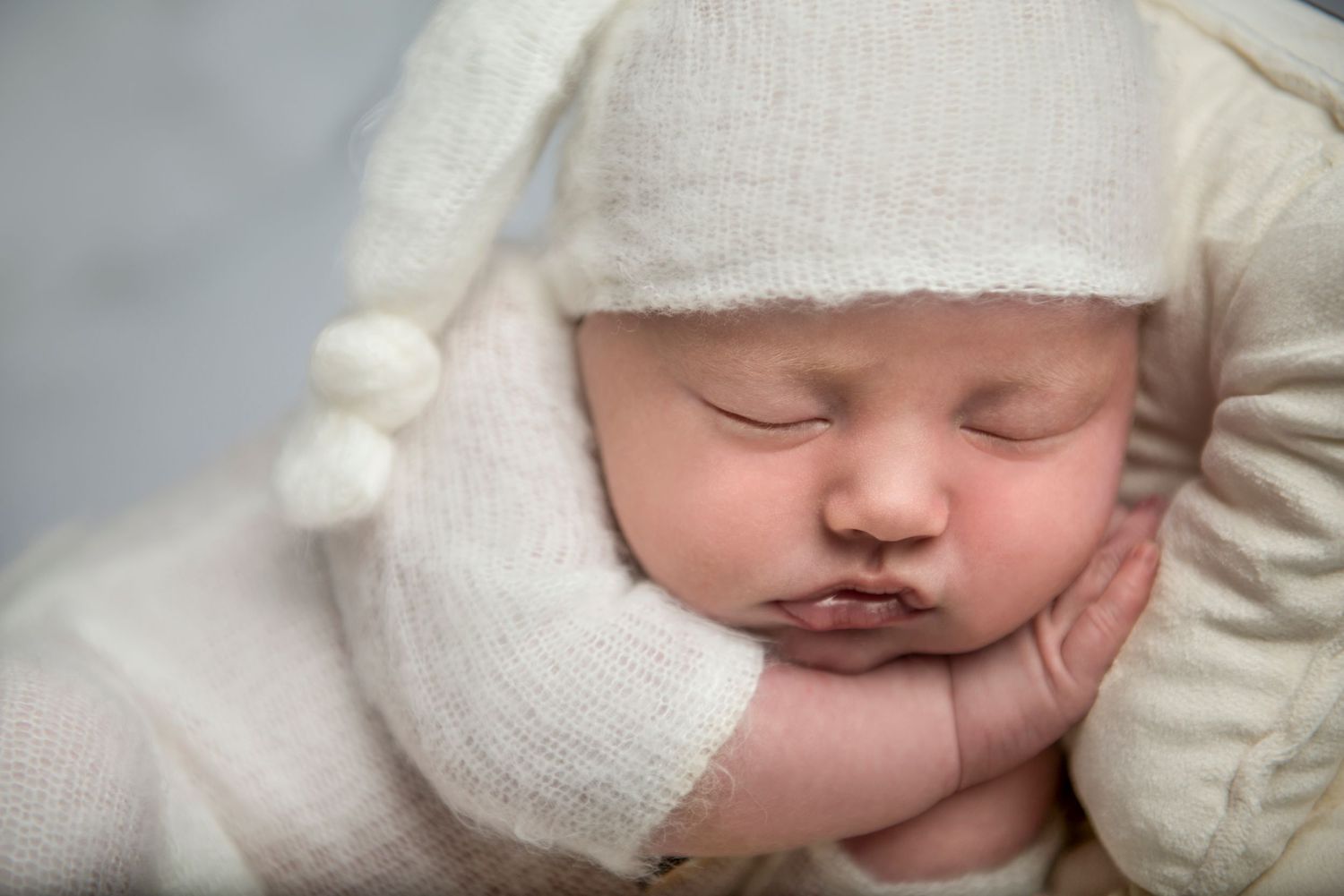 Serene sleeping newborn in white knit outfit against soft illuminated background.