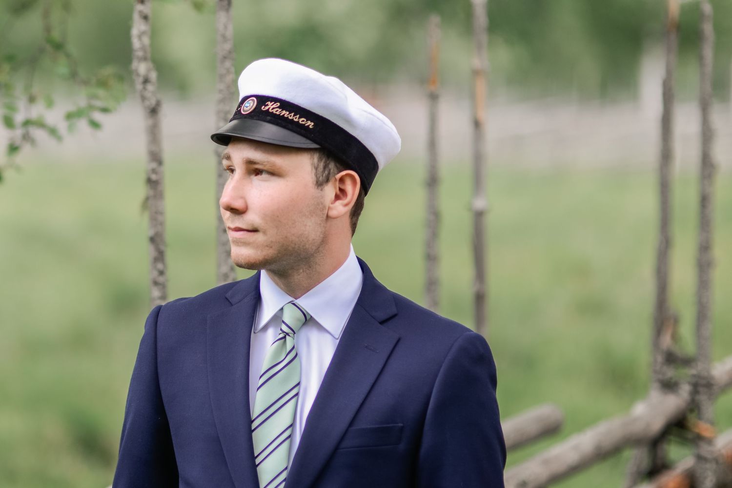 A person in a navy suit and striped tie poses outdoors with birch trees in the background.