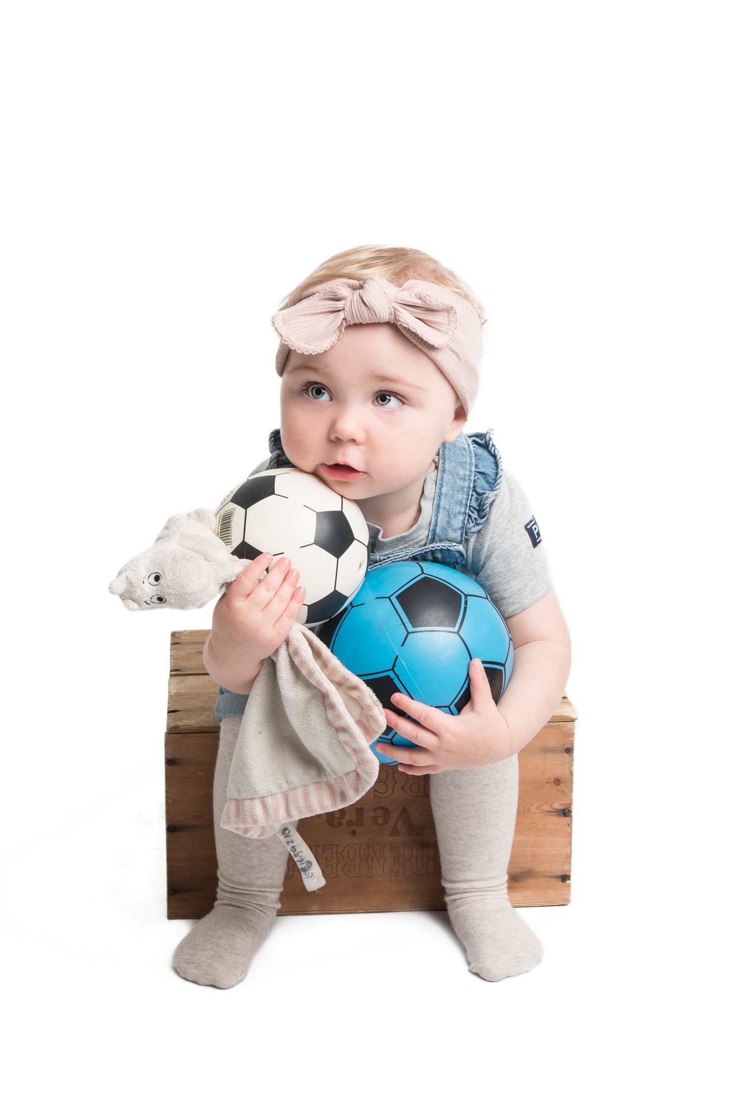 A child in denim and bow accessory poses with a blue and white soccer ball.