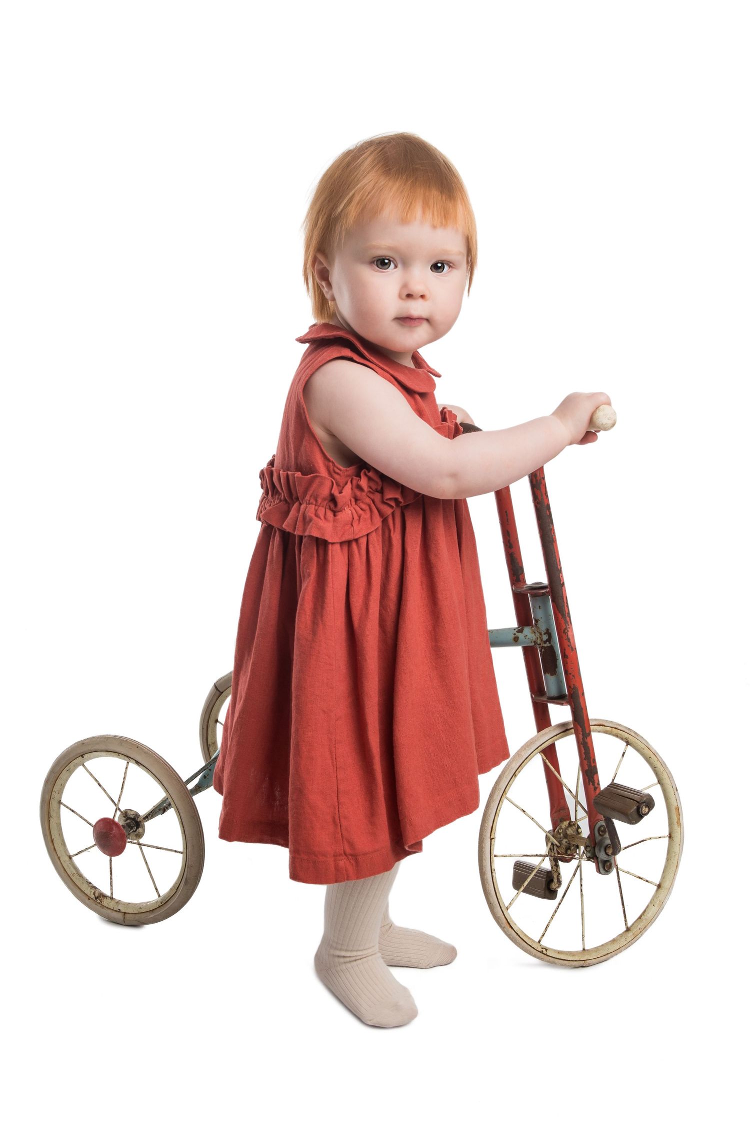Toddler in red dress plays with vintage wooden tricycle.