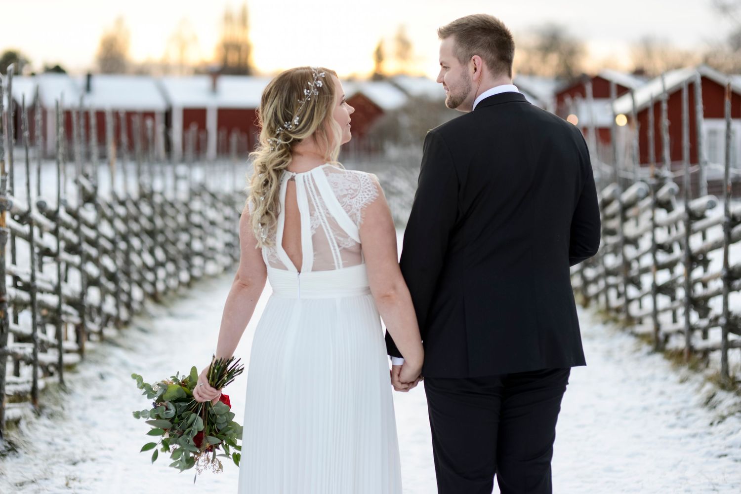 Snowy winter wedding scene with bride and groom against a rustic backdrop.