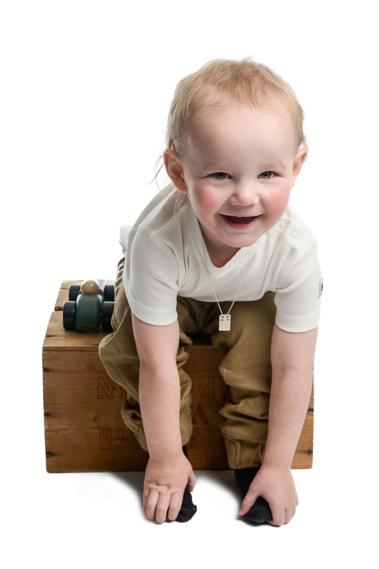 Smiling baby in white shirt crawling on wooden box against white background.