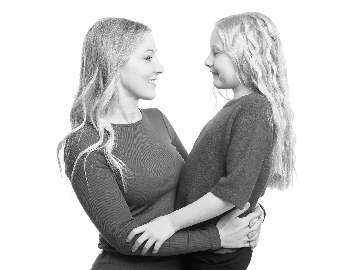 Mamma och dotter I svarta kläder omfamnar varandra delar ett ömt ögonblick i en svart vit fotoserie.