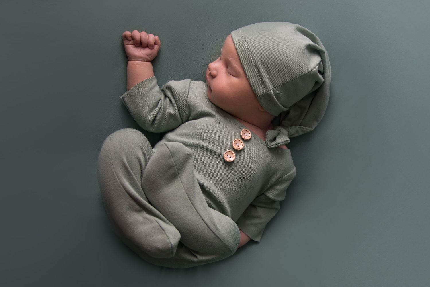 Baby in gray sleeper curled up during professional photo session.
