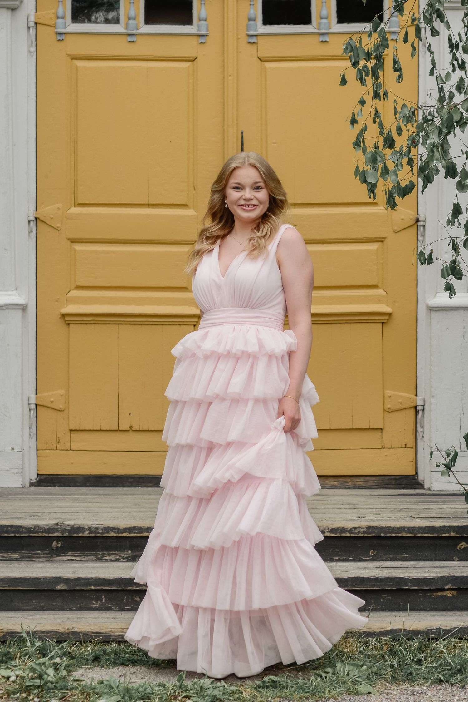 Woman in pink tiered dress poses in front of yellow doors in an outdoor setting.