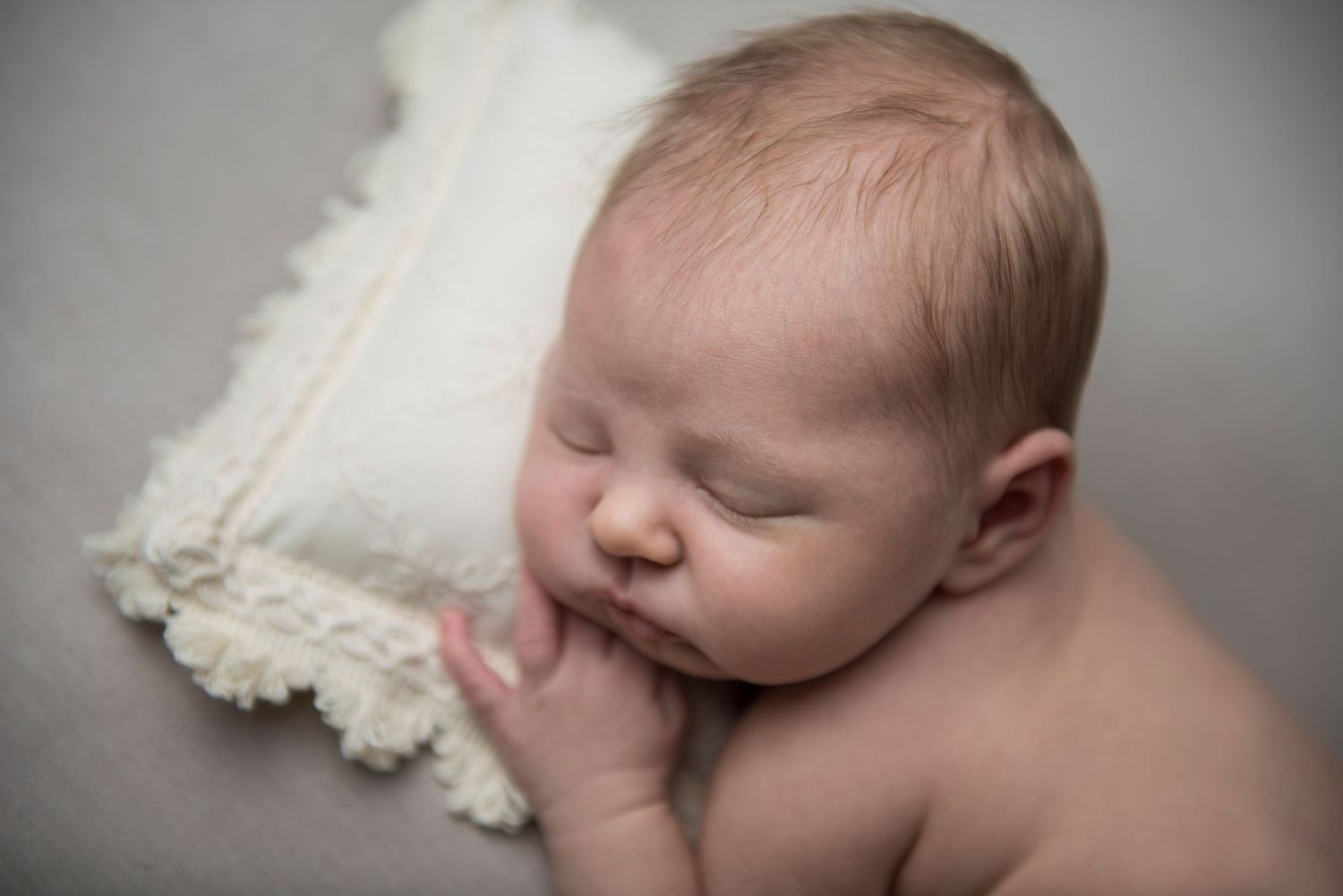 Newborn resting on white textured blanket in professional studio setting.