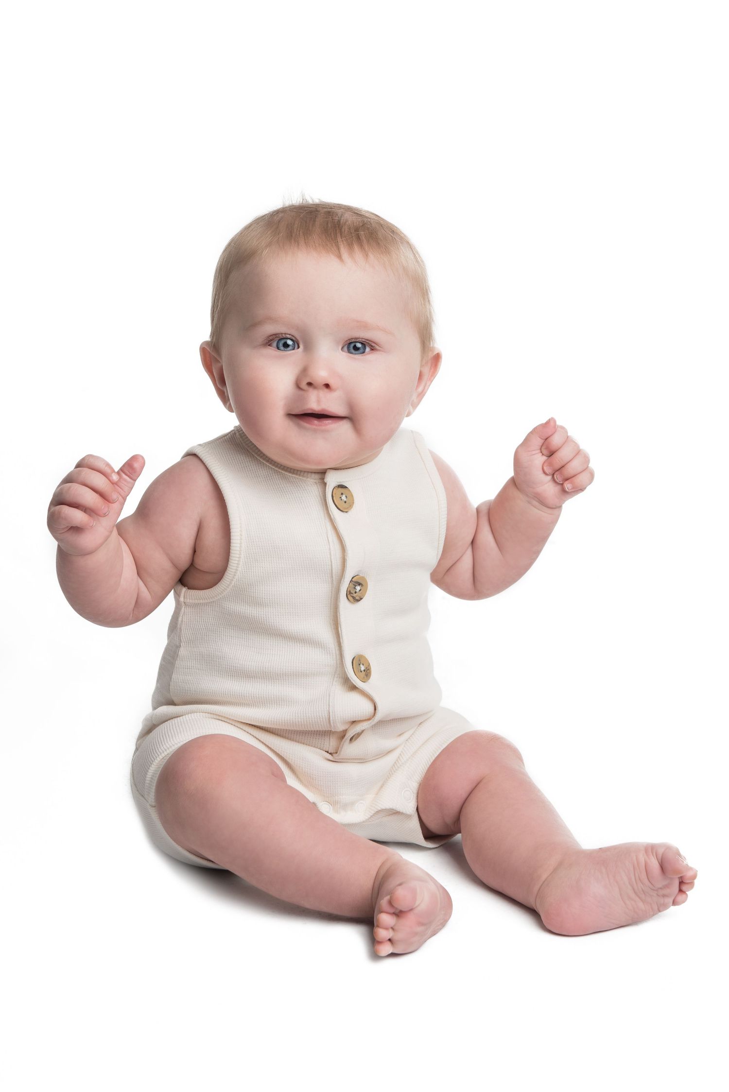 Baby in cream-colored romper with buttons sitting against white background.