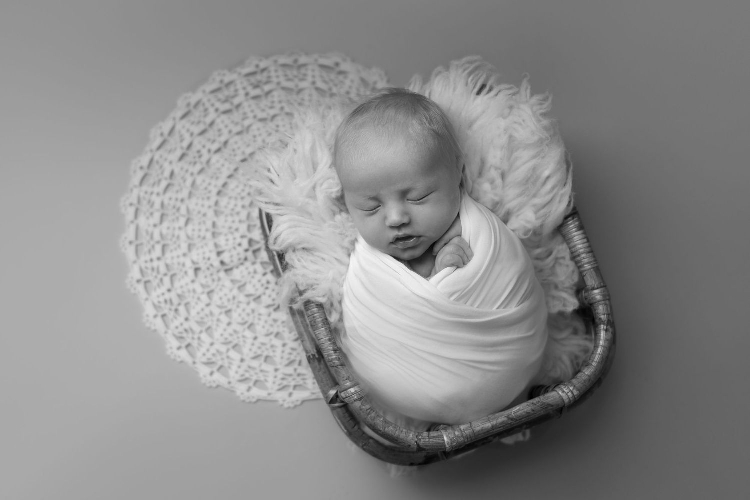 Newborn photography in black and white with delicate lace backdrop and woven basket.