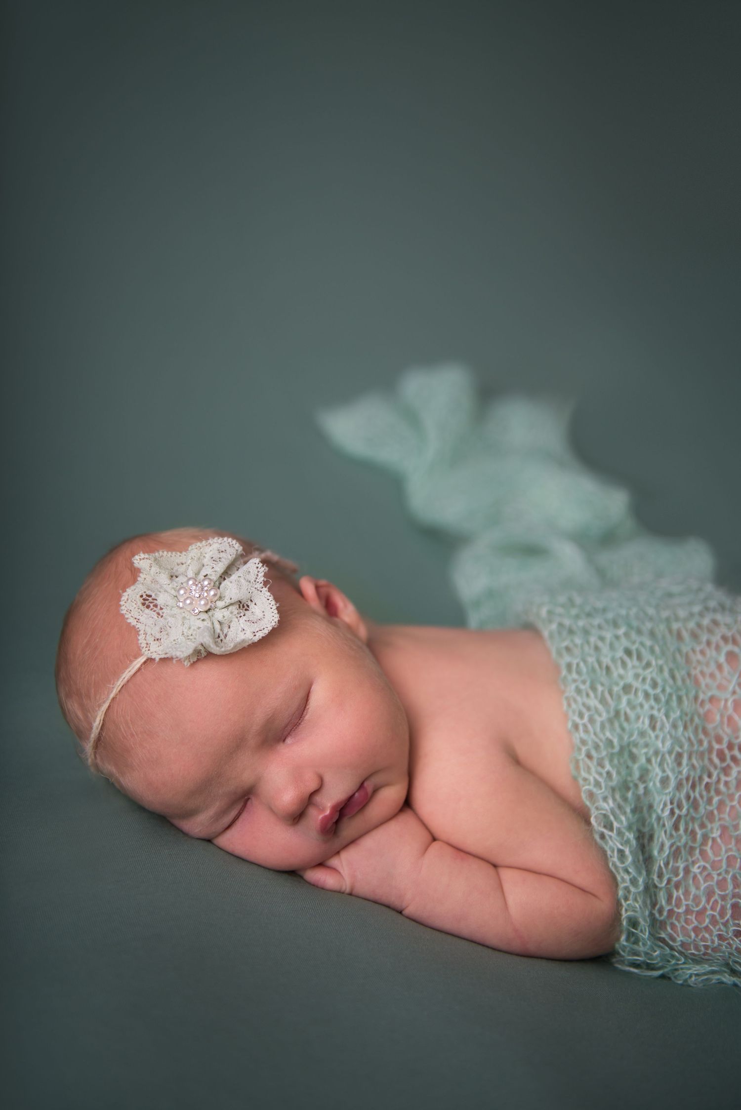 Sleeping newborn wearing delicate lace accessories on teal backdrop.