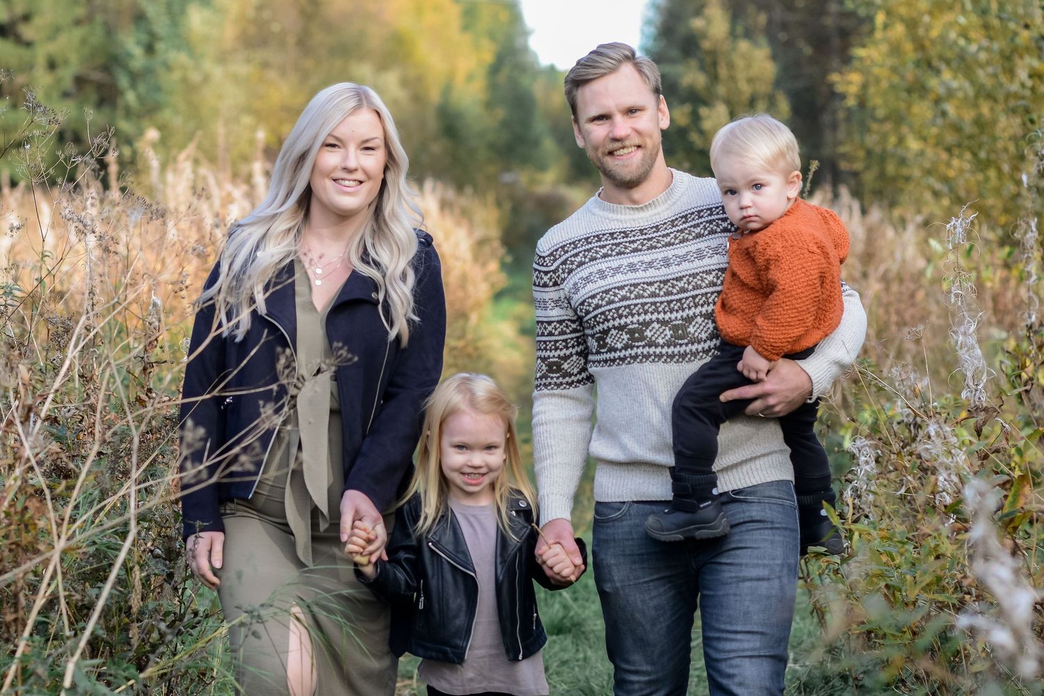 Happy family of four posing outdoors in autumn, parents with young daughter and baby boy among fall foliage.