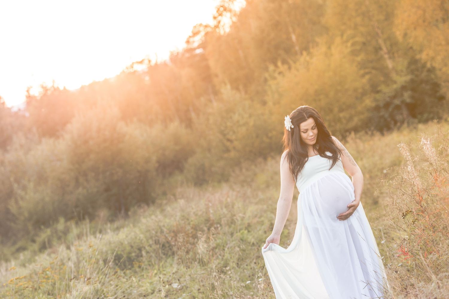 Ethereal maternity photoshoot in a golden field at sunset with flowing white dress.