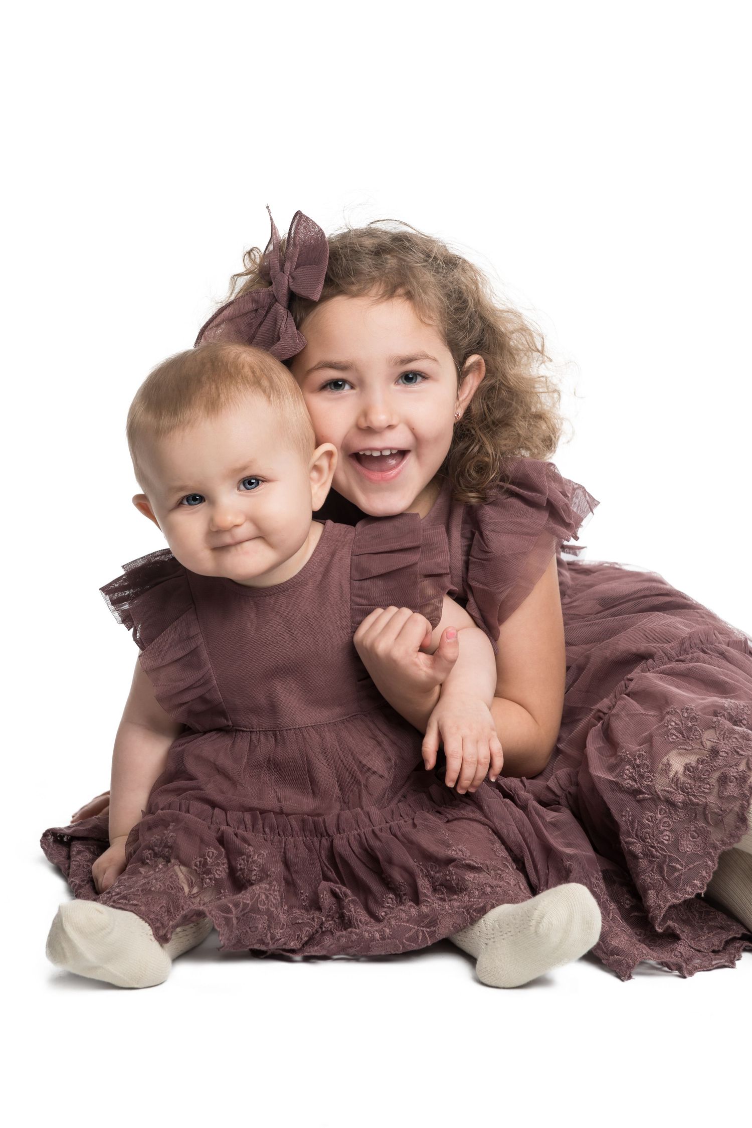 Two young children in brown dresses pose together for a portrait on white background.