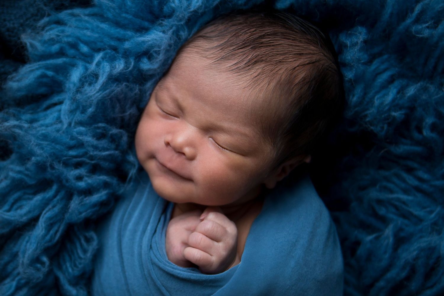 Newborn portrait series with deep blue textured fabric and moody lighting.