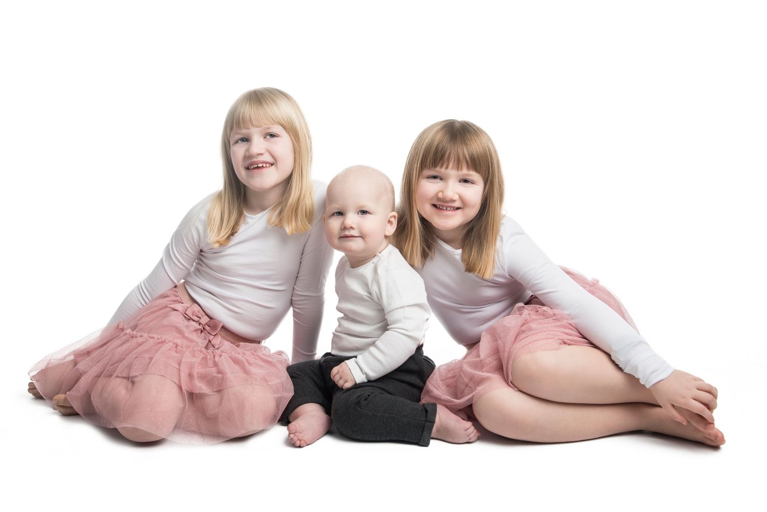Children in light colored outfits lying together on white background.