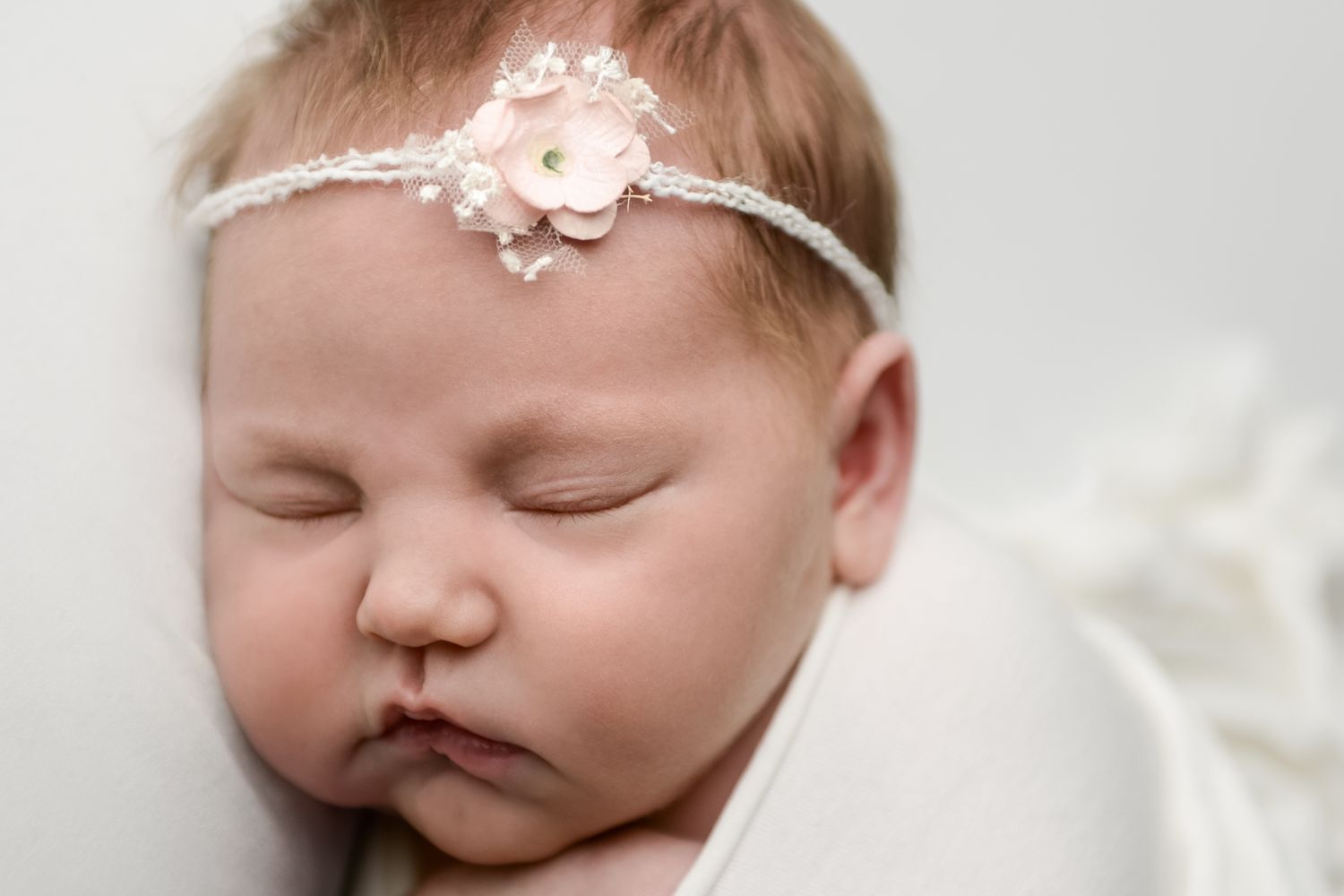 Delicate newborn portrait with lace headband and soft white tones.