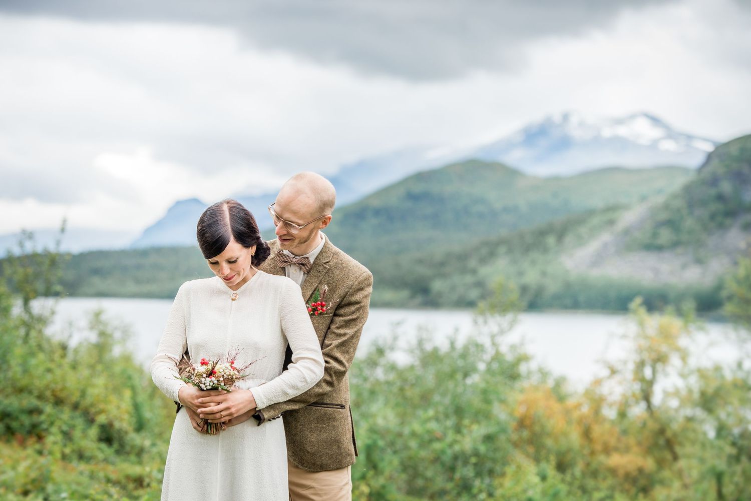 Couple shares a romantic moment on a hillside overlooking a mountain lake.