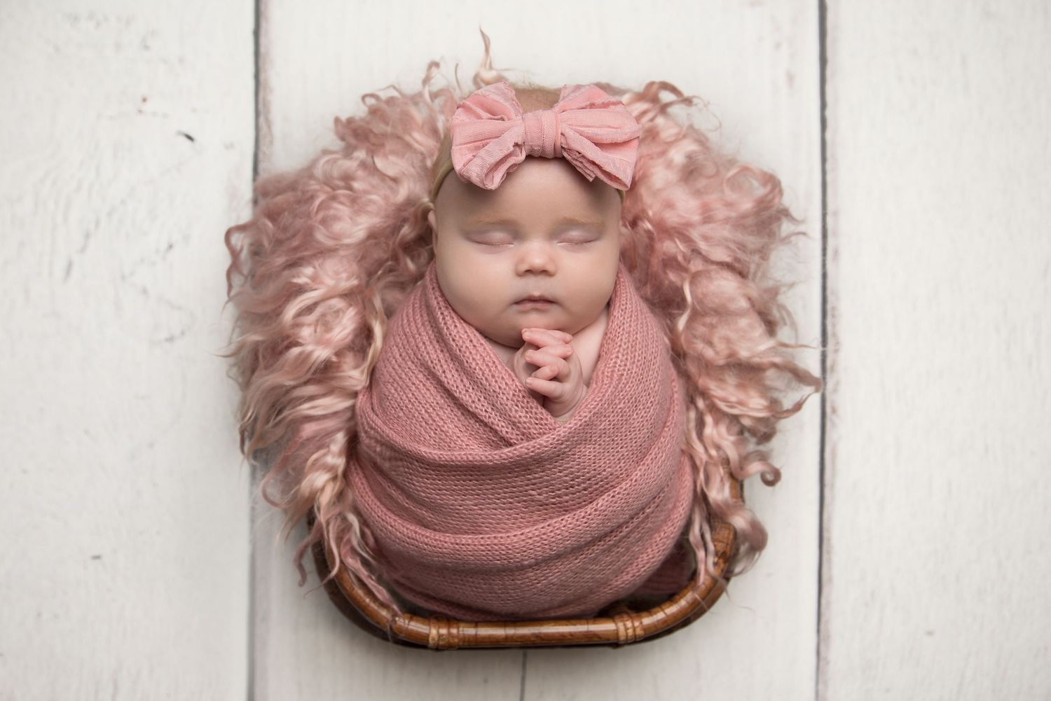 Artistic newborn portrait with baby wrapped in dusty rose fabric on white wooden floor.