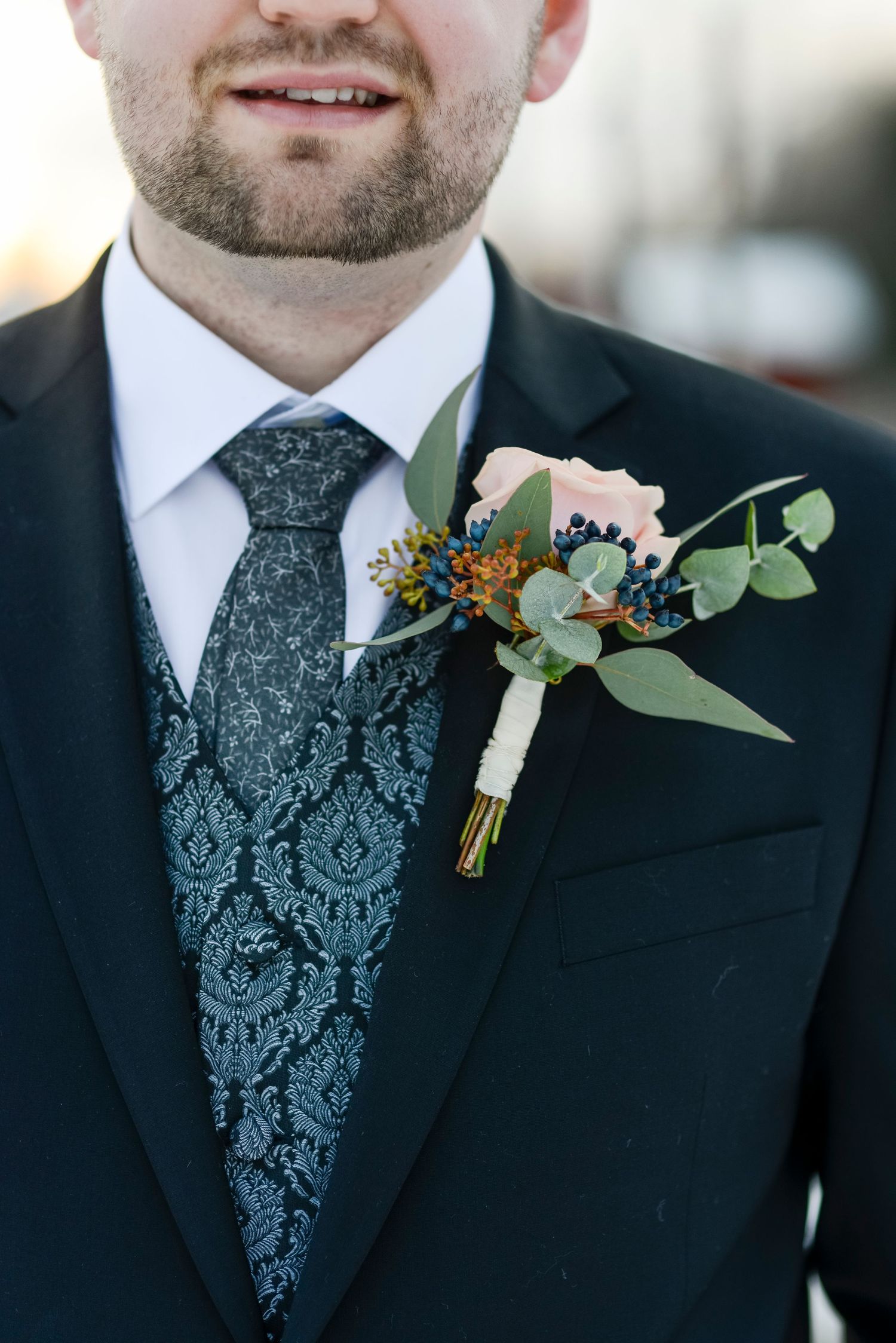 Close-up of boutonniere with eucalyptus and flowers on black suit lapel.