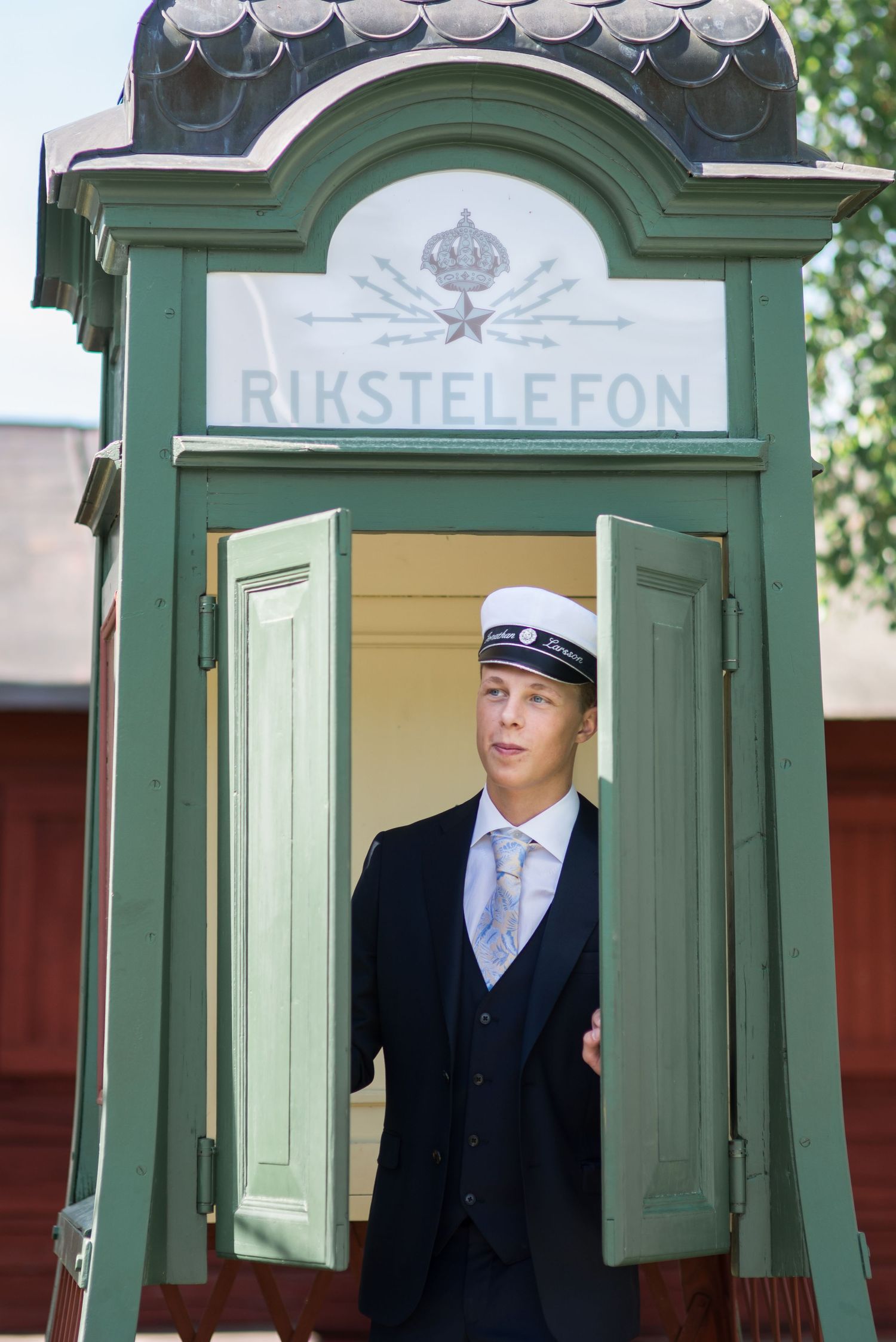 A vintage green telephone booth marked 'Rikstelefon' with someone in formal attire.