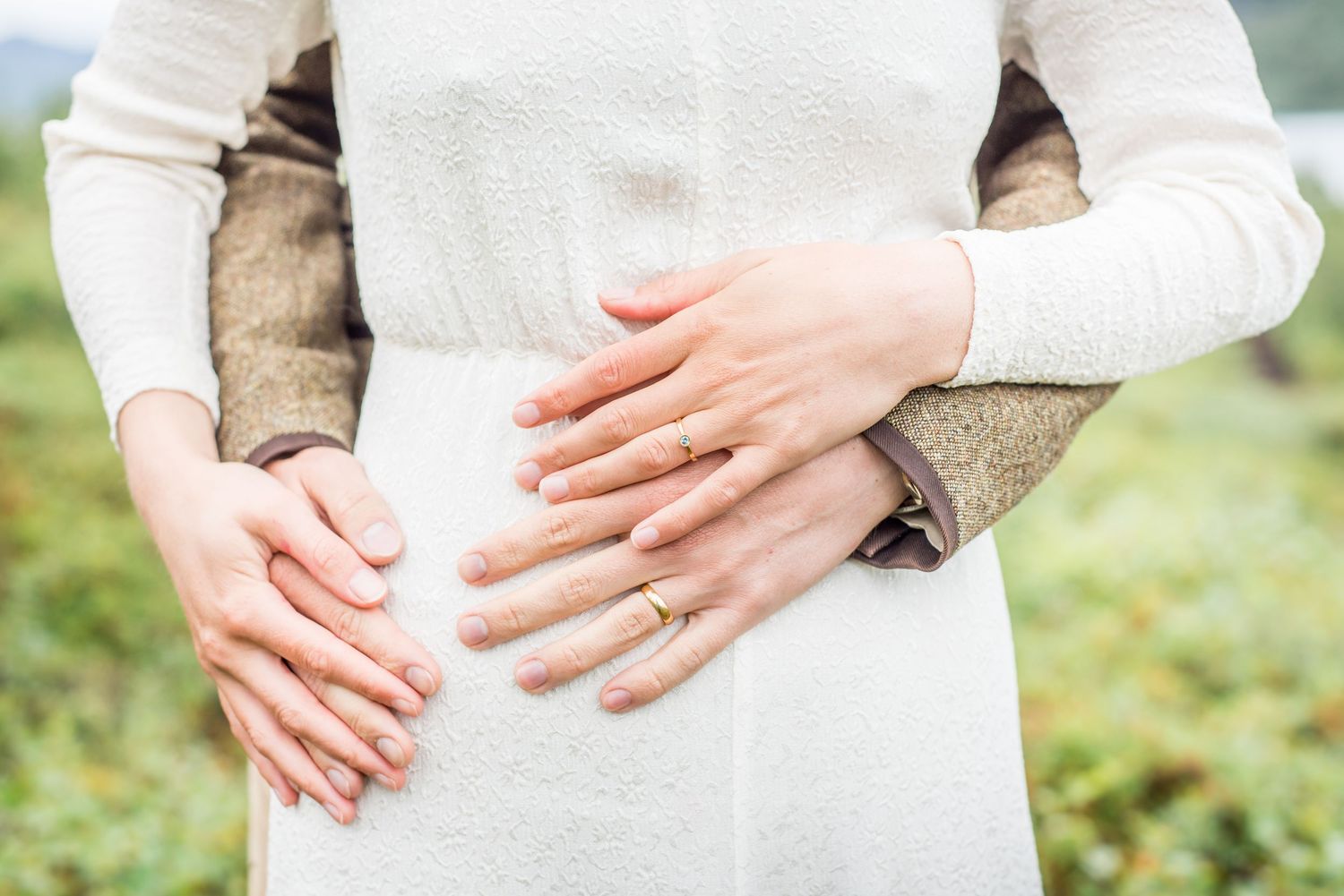 Close-up of hands showing wedding rings against a white dress.
