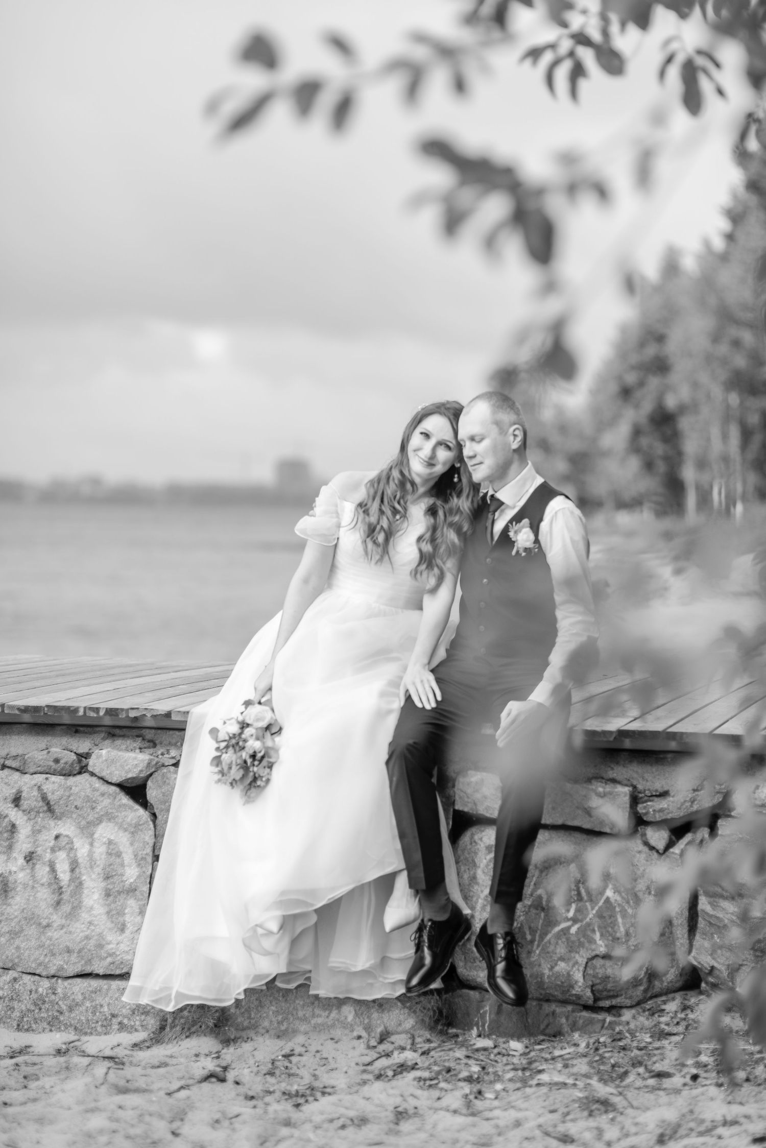 Wedding couple sitting together on rustic stone wall with dreamy background.
