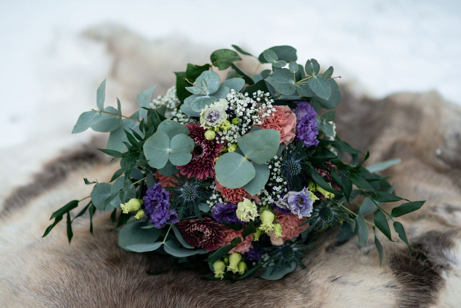 Colorful wedding bouquet with eucalyptus, purple flowers, and greenery arranged on snow.