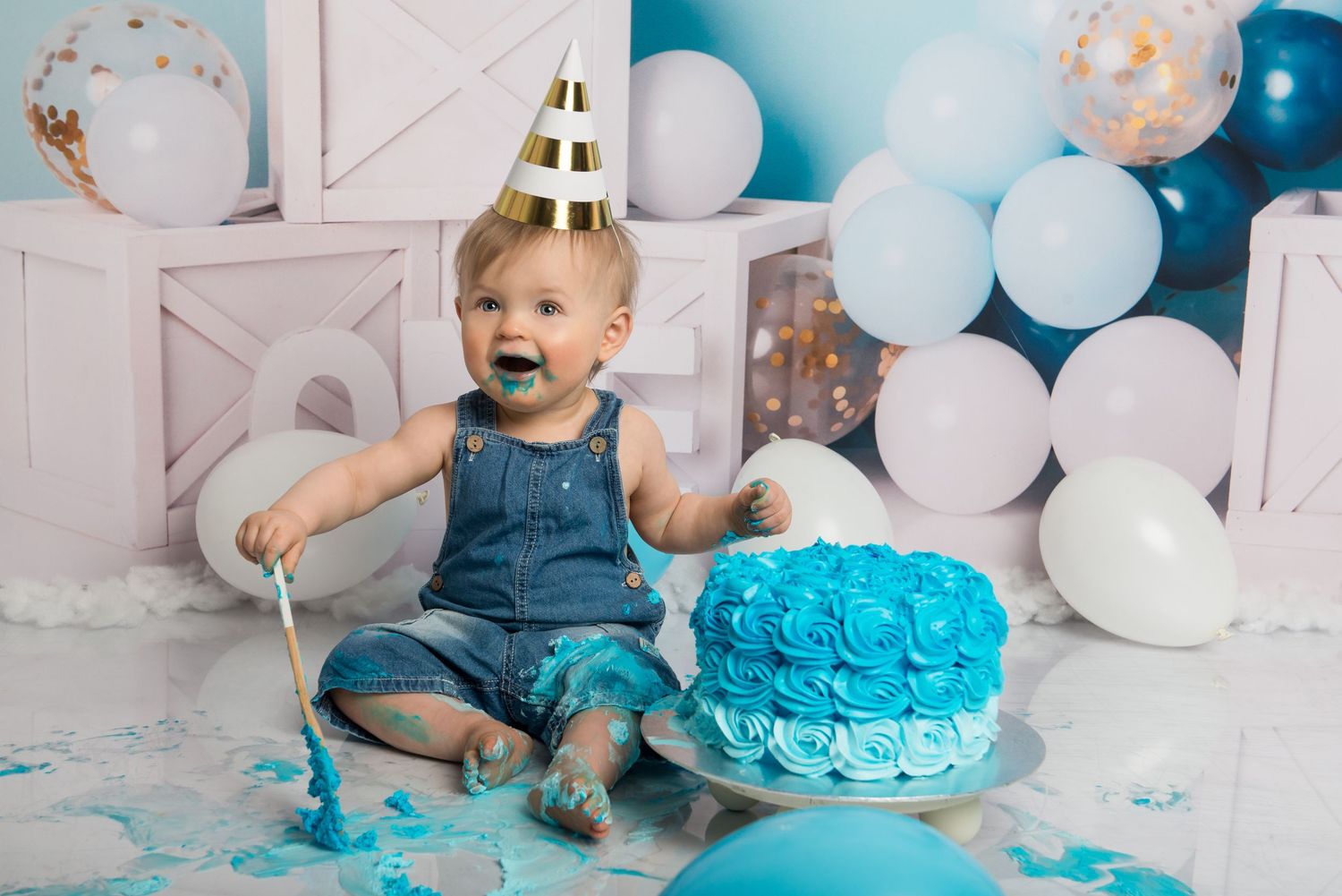A cake smash photoshoot with bright blue frosting and scattered balloons creating a joyful celebration scene.