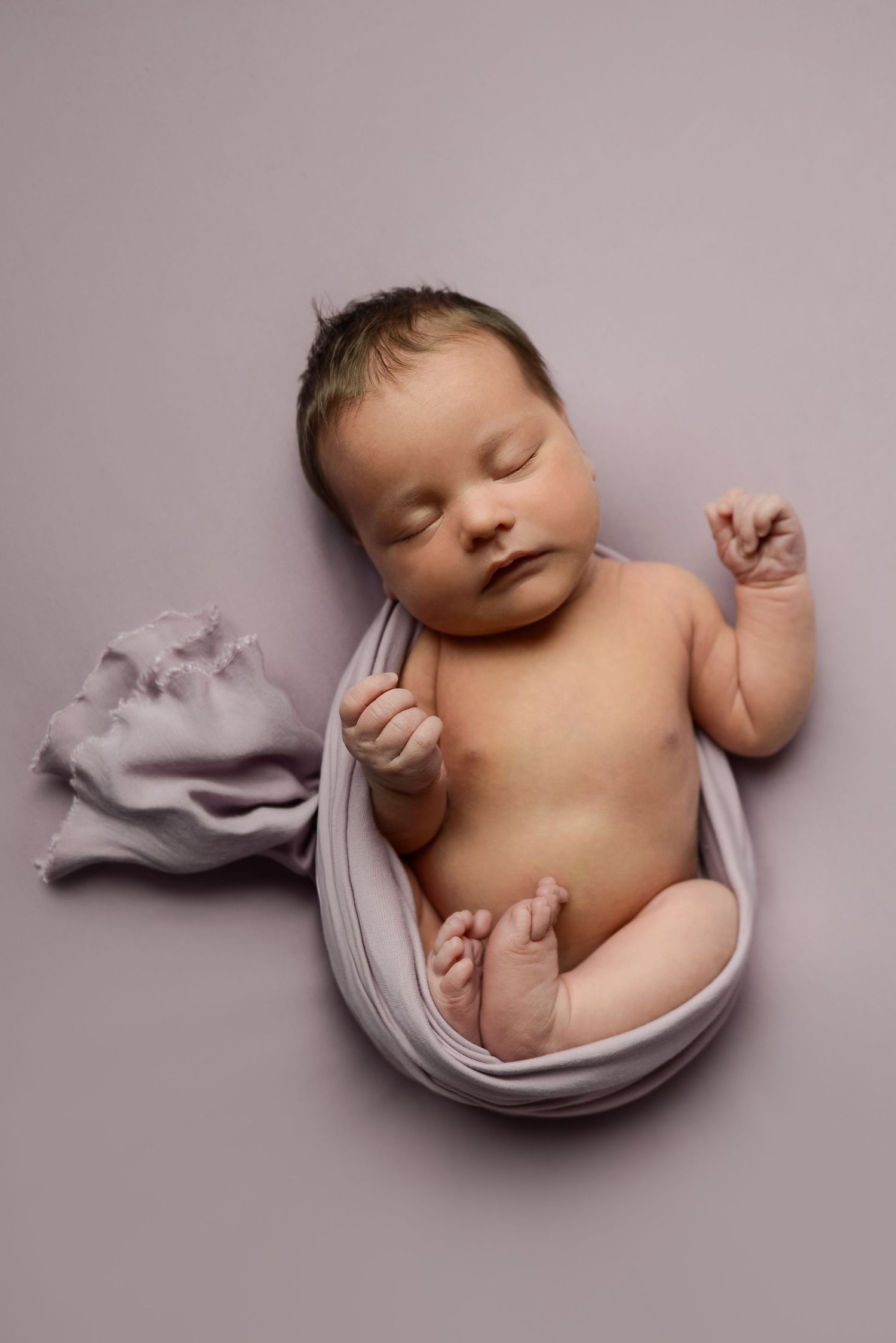Simple studio portrait of sleeping newborn with gentle fabric draping on grey background.
